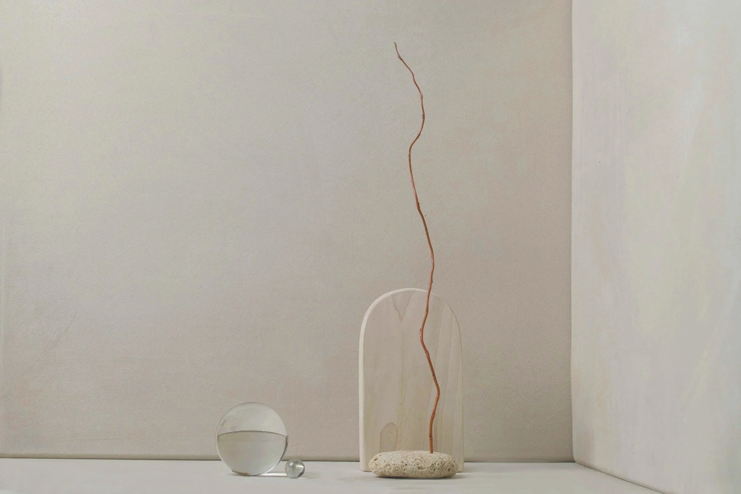 Minimalist arrangement with decorative spheres, a stone, a thin plant stem, and white and beige background.