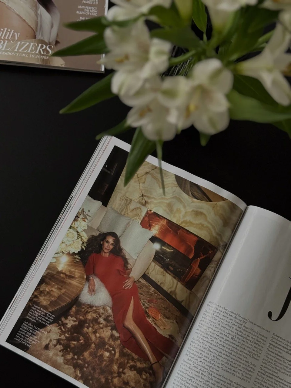 Open editorial magazine spread with white flowers on a dark table, representing press coverage and earned media secured by Brand Curators.