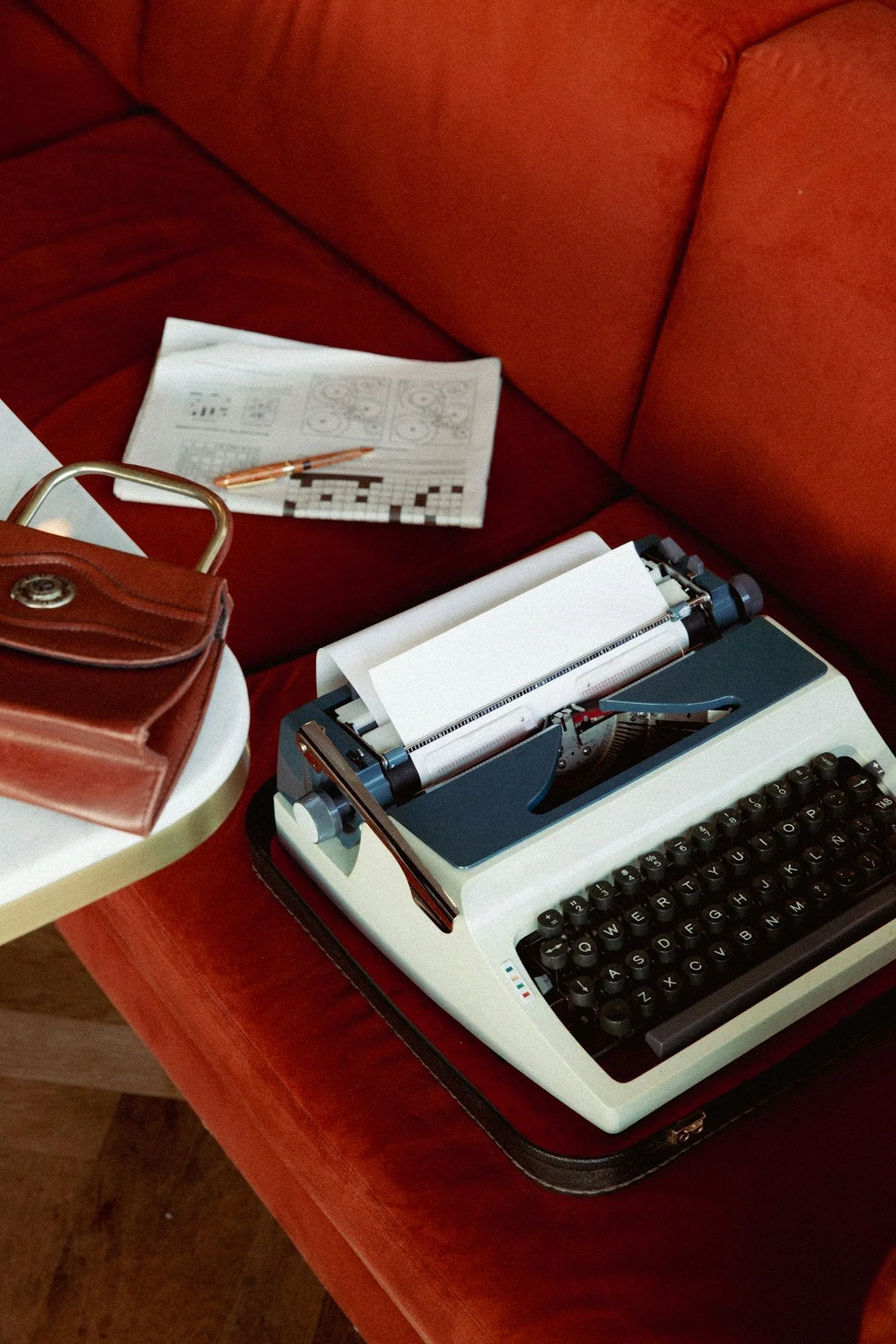 Vintage typewriter on a red velvet sofa with a leather bag and newspaper, representing the storytelling approach behind Brand Curators' strategic communications