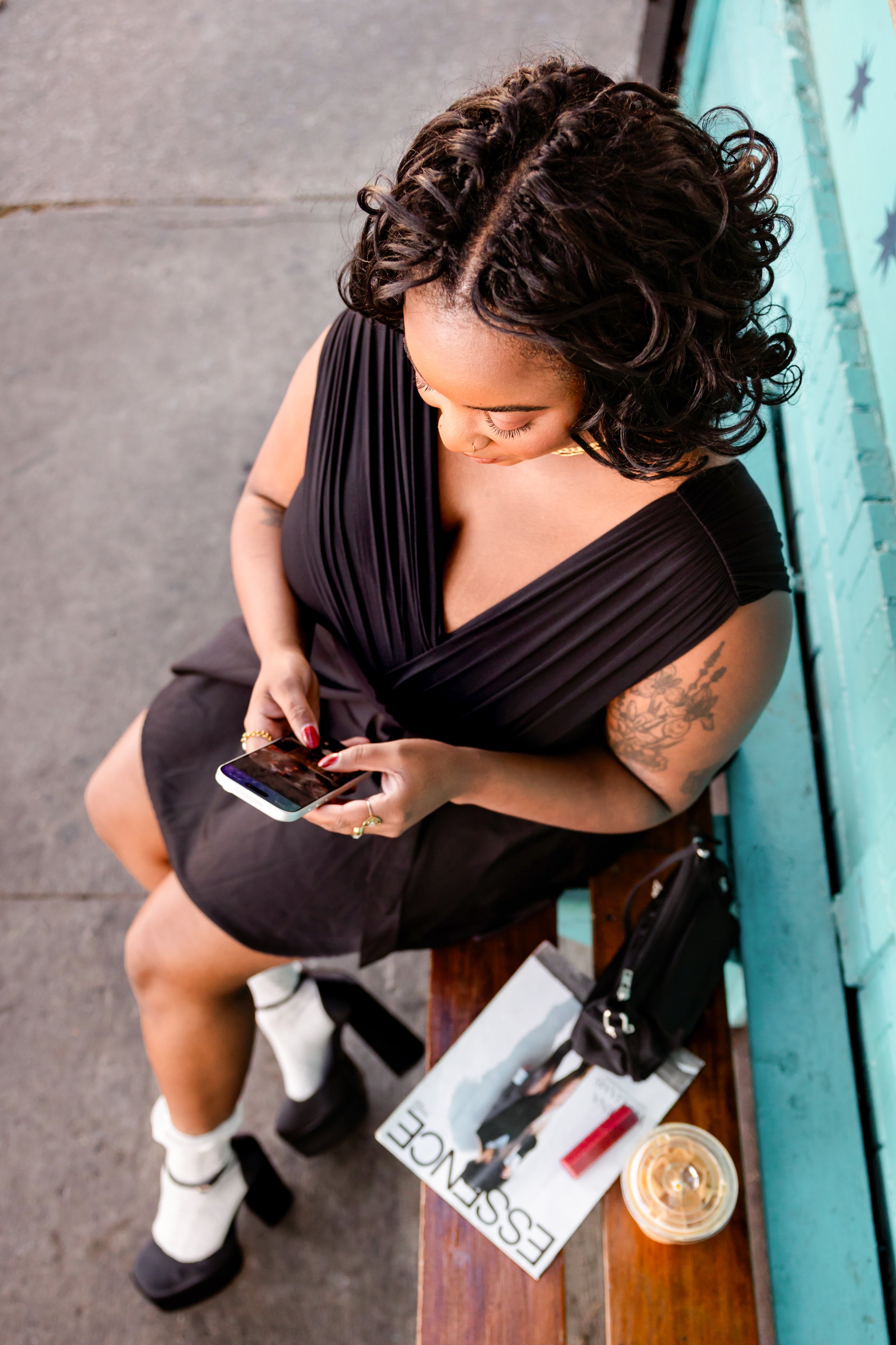 Brand Curators founder Tiffany Knighten reviewing creator content on her phone, with Essence magazine nearby, representing hands-on talent management in the creator economy