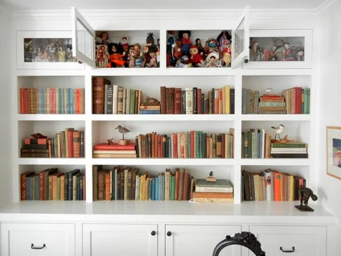 In the library, books, artifacts and a doll collection share the shelves. (Copy)