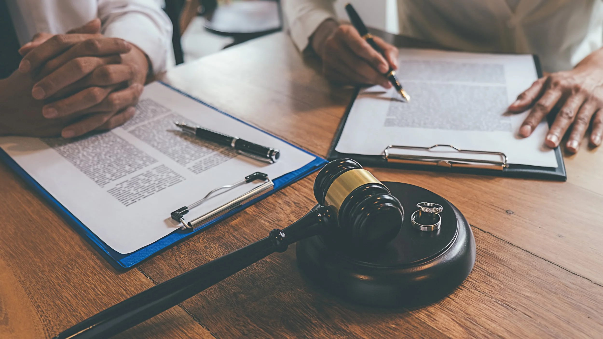 A courtroom scene with a judge's gavel, legal documents on clipboards, and rings on a stand, indicating a legal setting.