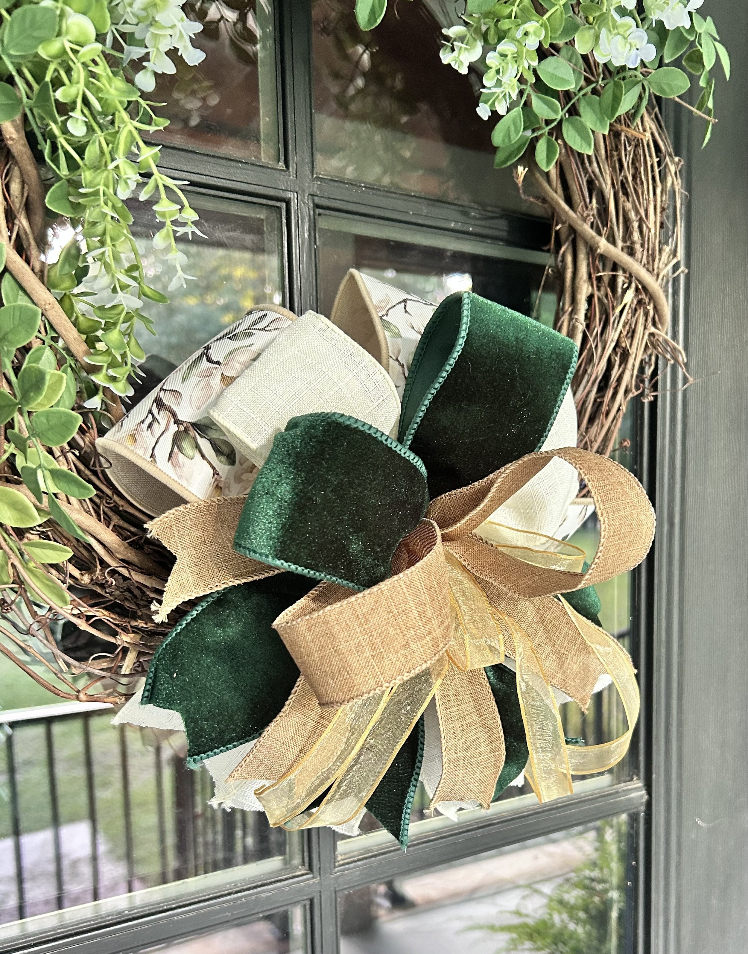 Magnolia Petite Bow with green velvet, magnolia floral ribbon, natural linen and gold accents displayed on a grapevine wreath