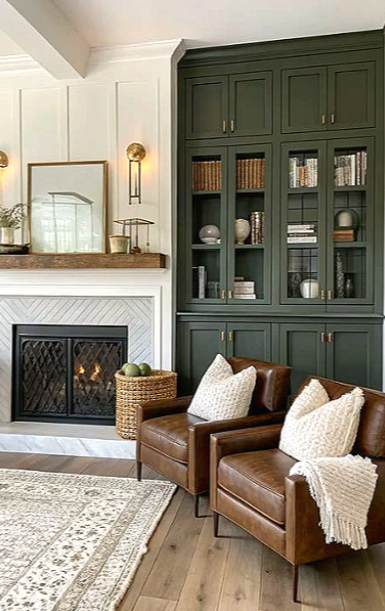 Living room corner with a fireplace, white and green built-in shelves, and brown leather armchairs with white pillows.