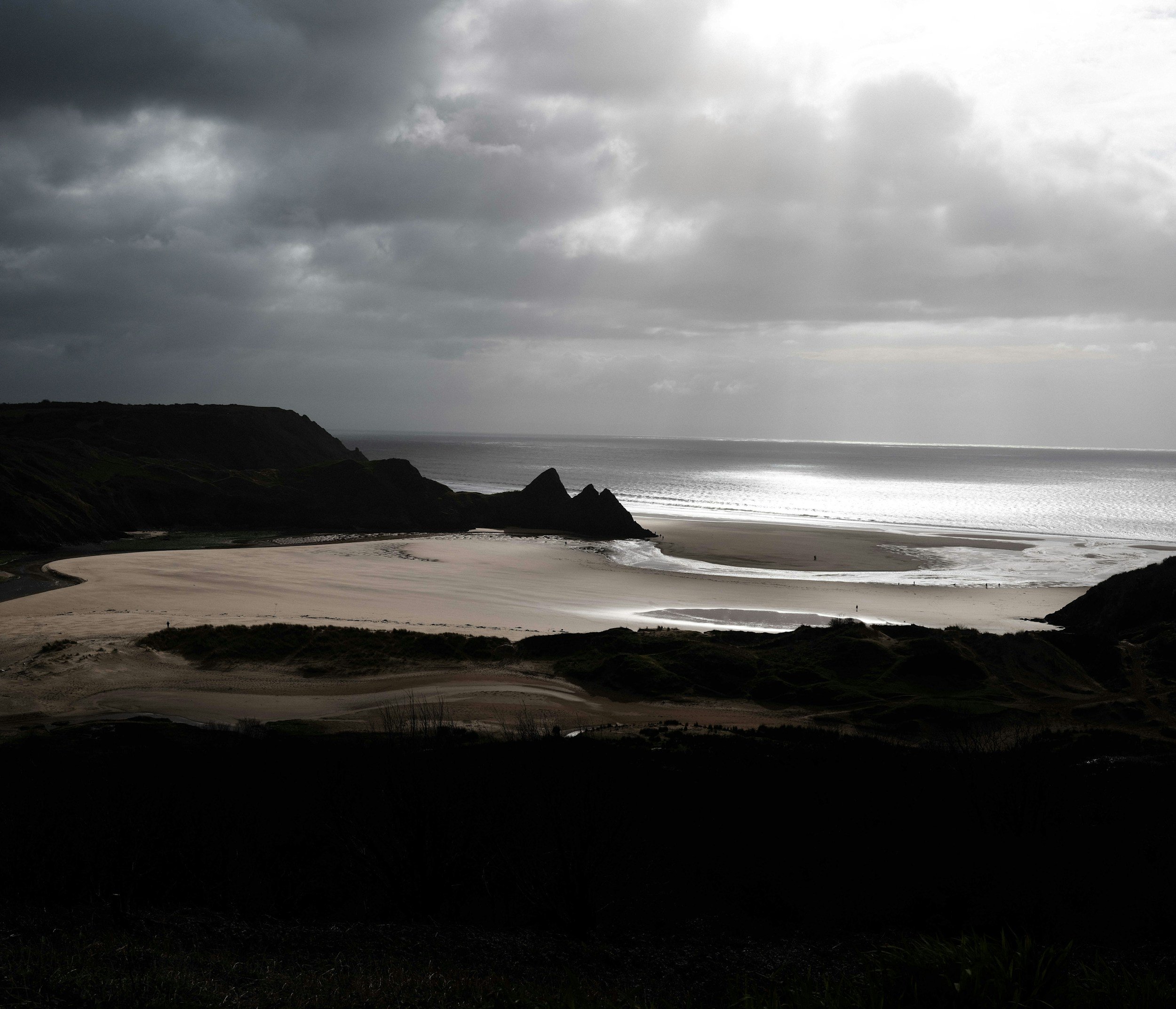 Dark, cloudy sky over a coastal landscape with cliffs, beach, and the ocean on a cloudy day.