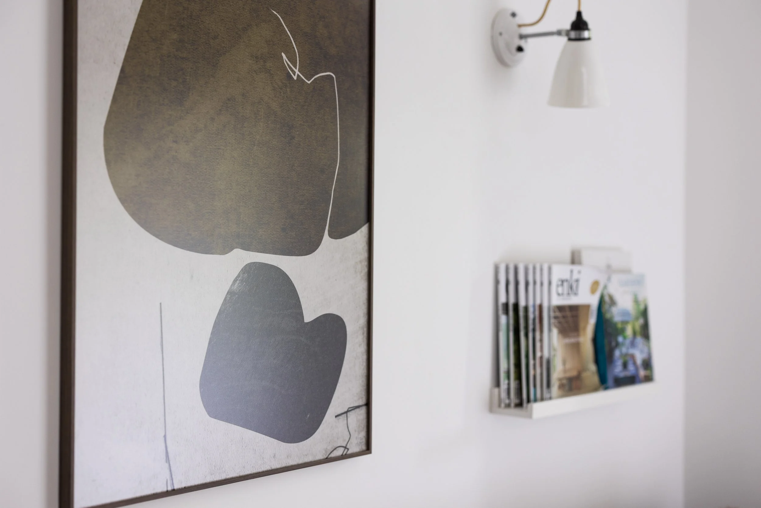 Close-up view of abstract wall art with bold colors, shapes, and lines, mounted on a wall in a room with a white wall socket and a bookshelf with books in the background.
