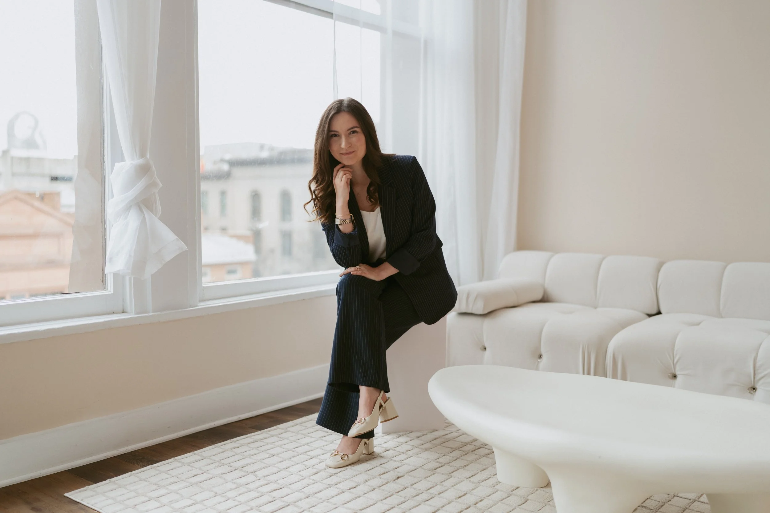 Danielle sitting on the armrest of a couch in a navy blazer.