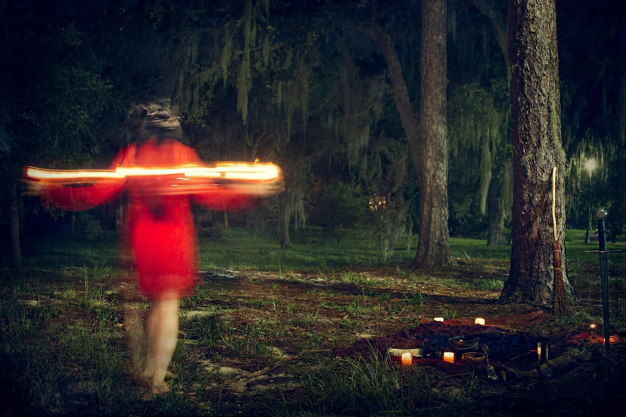 A women in a red dress walking through a dark forest at night, with blurred motion and light streaks from her movement.