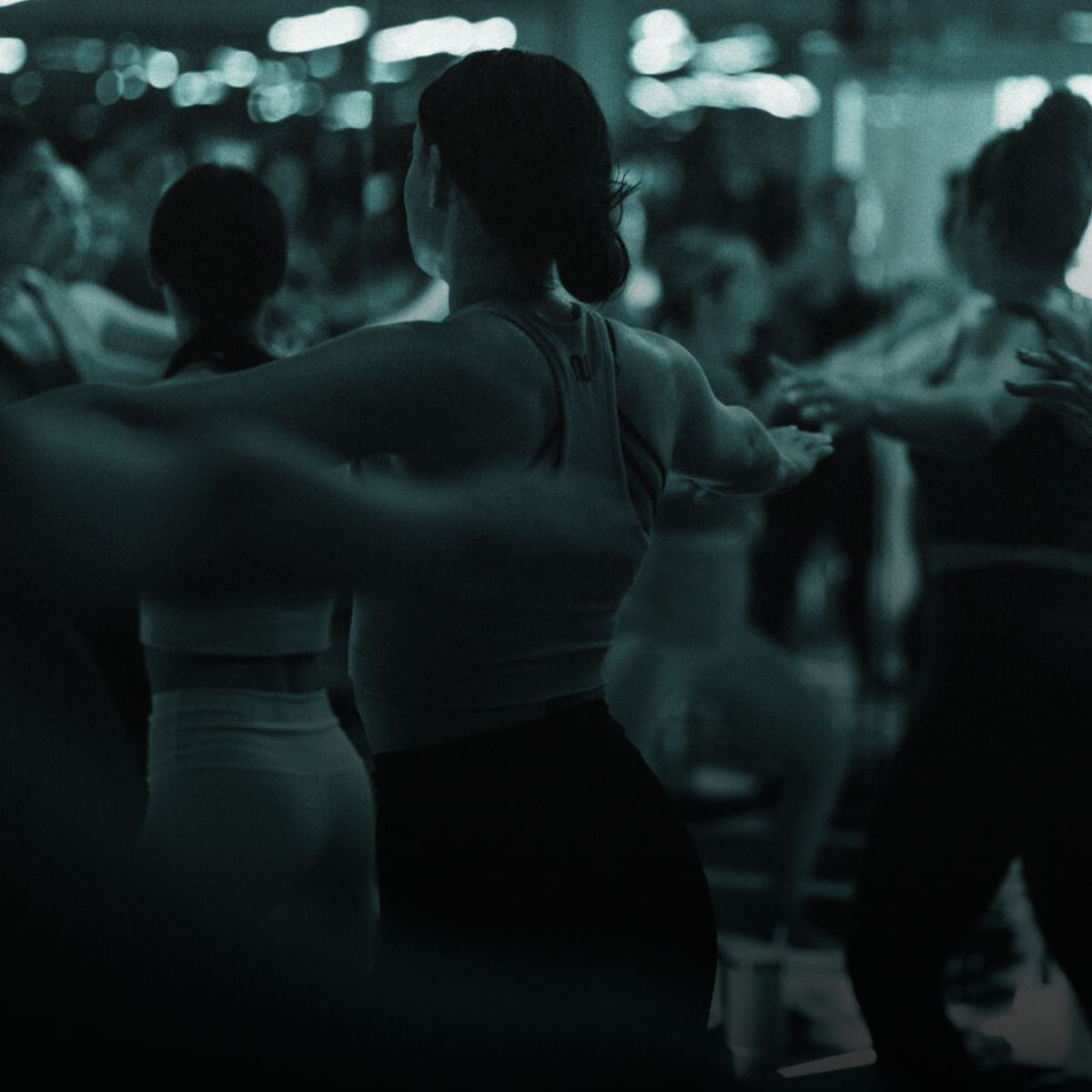 A woman in athletic clothing stretching in a crowded gym or fitness class.