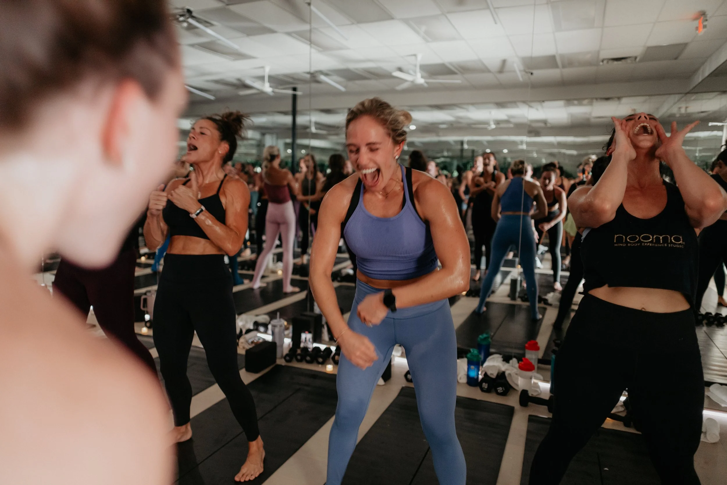 Group of women participating in a lively fitness class in a gym, laughing and enjoying the workout.