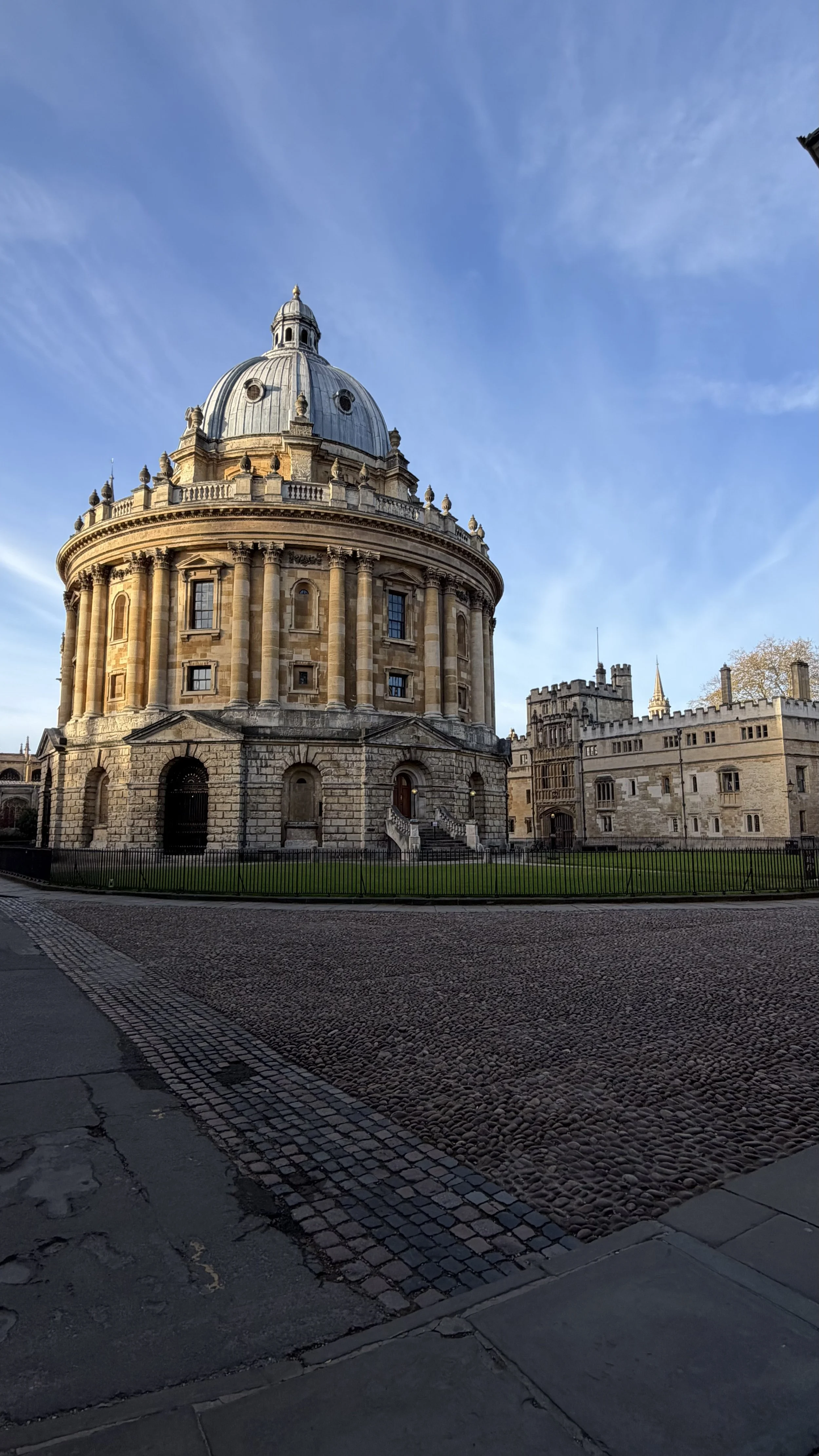 A historic round building with a domed roof, stone steps, and small windows, located on a cobblestone street under a clear blue sky.