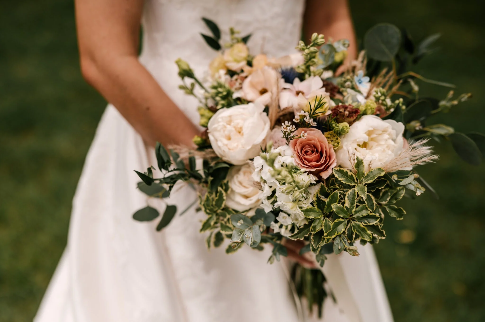 A bride white dress holding a bouquet of assorted flowers and greenery outdoors.