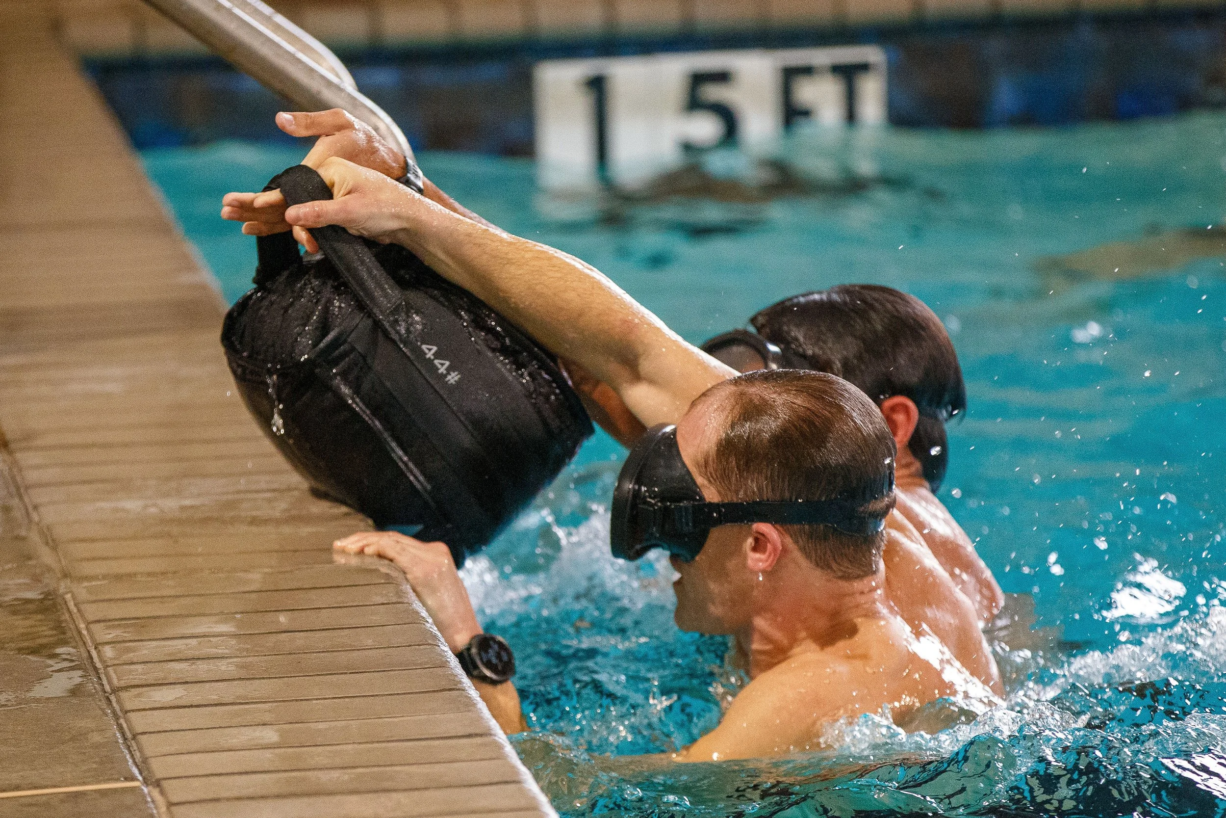 Swimmers in the pool gripping and assisting each other at the edge of the pool during a swim practice or competition.