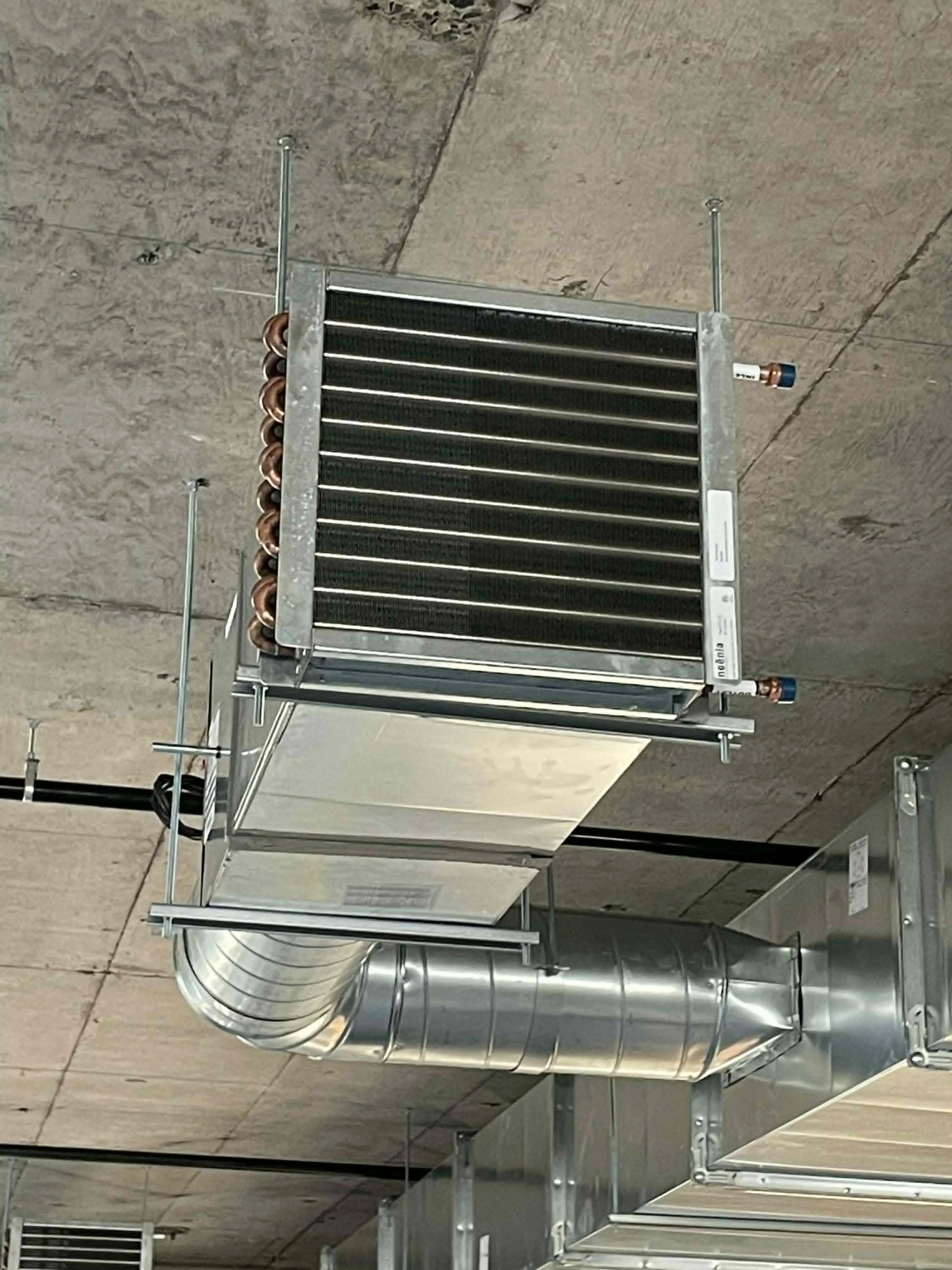 Vue d'une installation de conduits de ventilation en montant, avec des tuyaux en métal, dans un bâtiment industriel ou commercial.