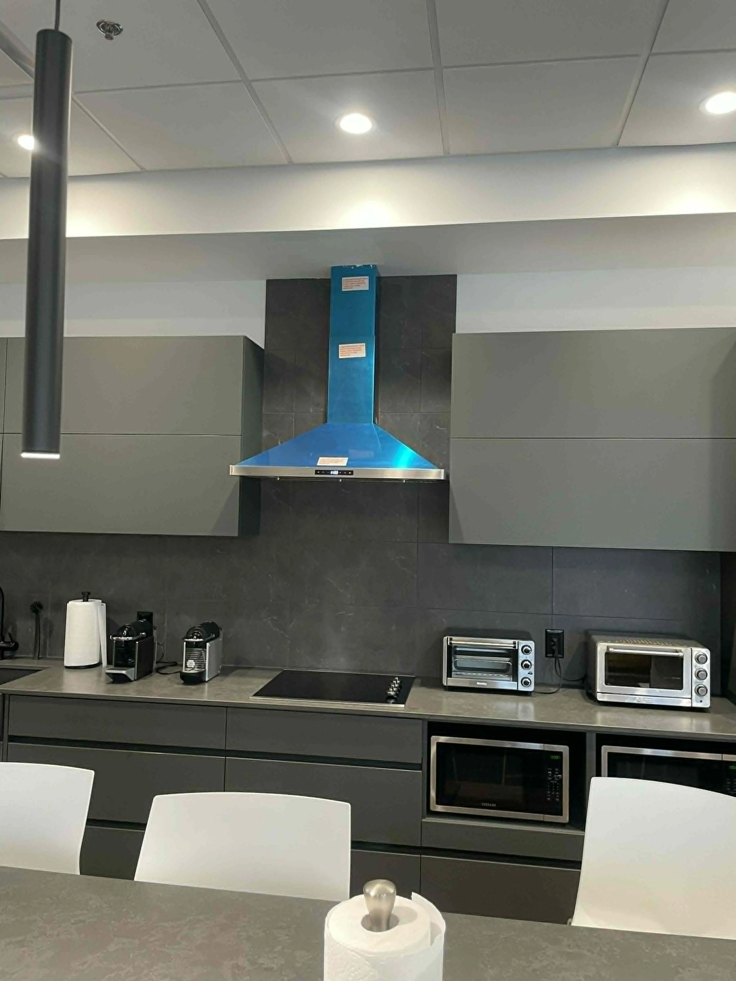 Cuisine moderne avec des appareils électroménagers, un plan de travail en pierre, et des fauteuils blancs.