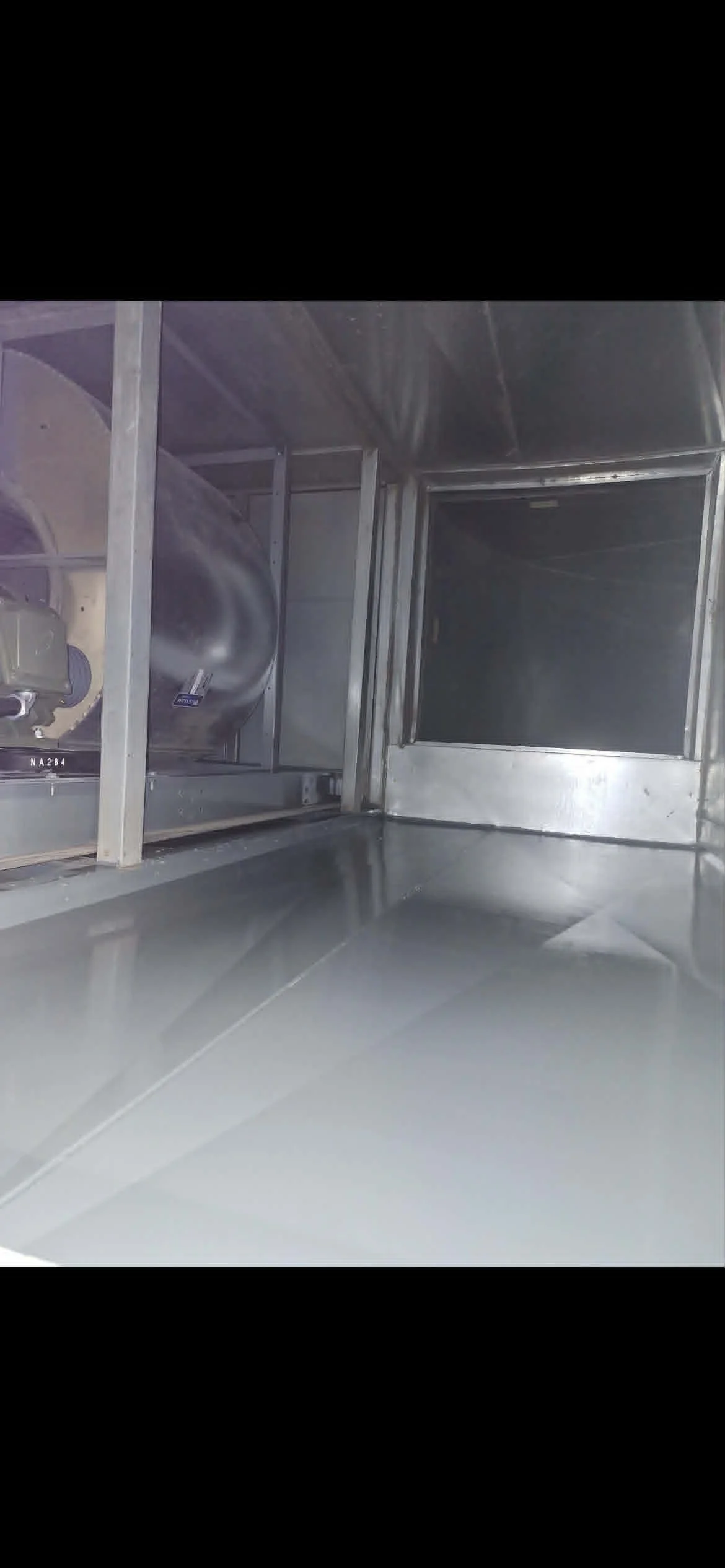 Intérieur d'une cuisine en acier inoxydable avec un grand espace vide et un équipement partiellement visible à gauche.