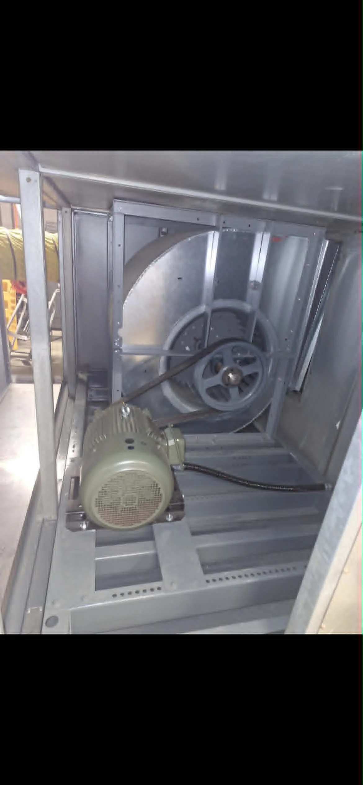 Une machine ou un équipement en acier inoxydable avec un moteur électrique gris attaché. La machine possède un grand tambour ou un coffre avec une roue visible à l'intérieur.