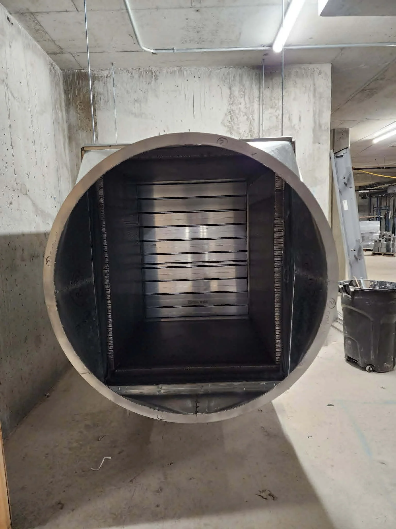 Un tunnel en acier inoxydable avec un intérieur noir et des bandes horizontales, probablement un four industriel, situé dans une zone industrielle ou un entrepôt.