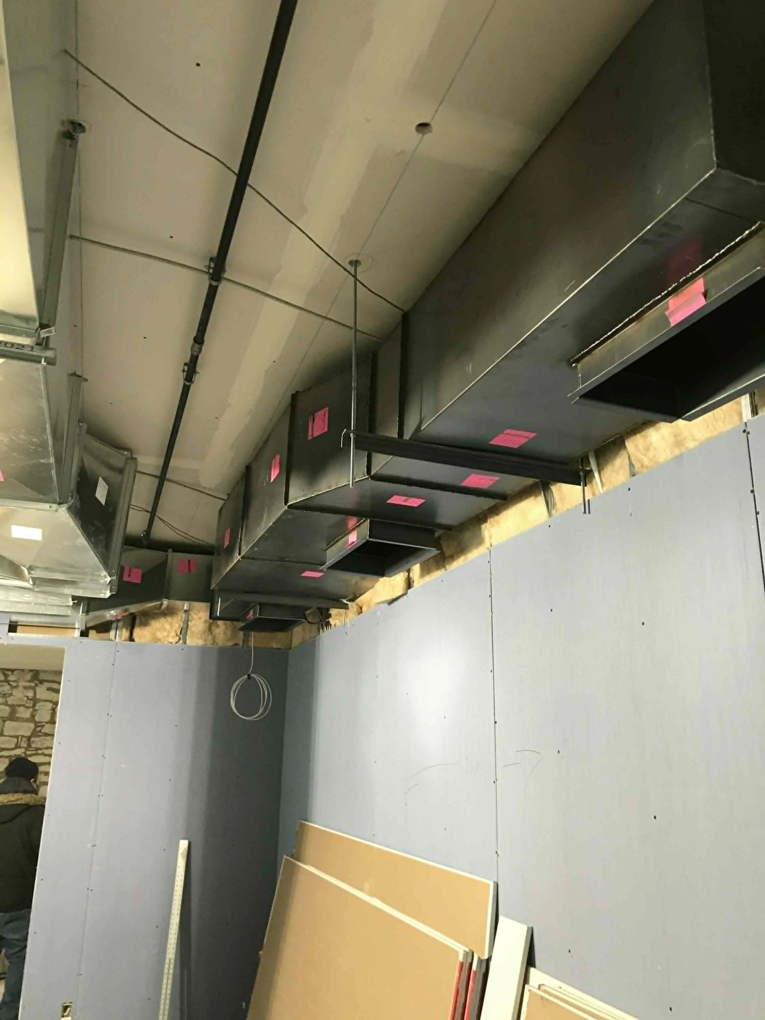 Construction d'une cuisine avec des armoires en cours d'installation, plusieurs panneaux de bois, un sol en carrelage gris, et des éléments en métal fixés au plafond.