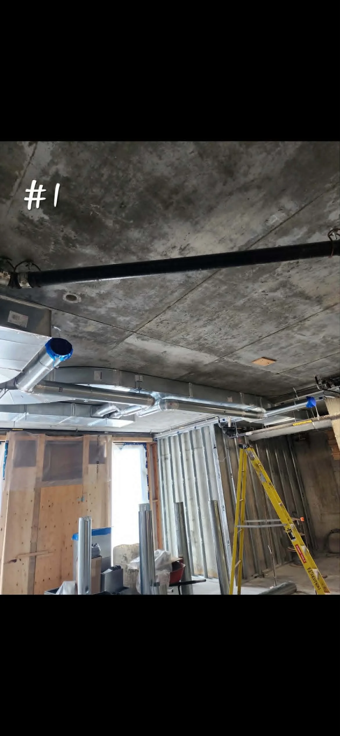 Construction intérieure avec des conduits en métal, une échelle, des murs en chantiers et un plafond en béton.