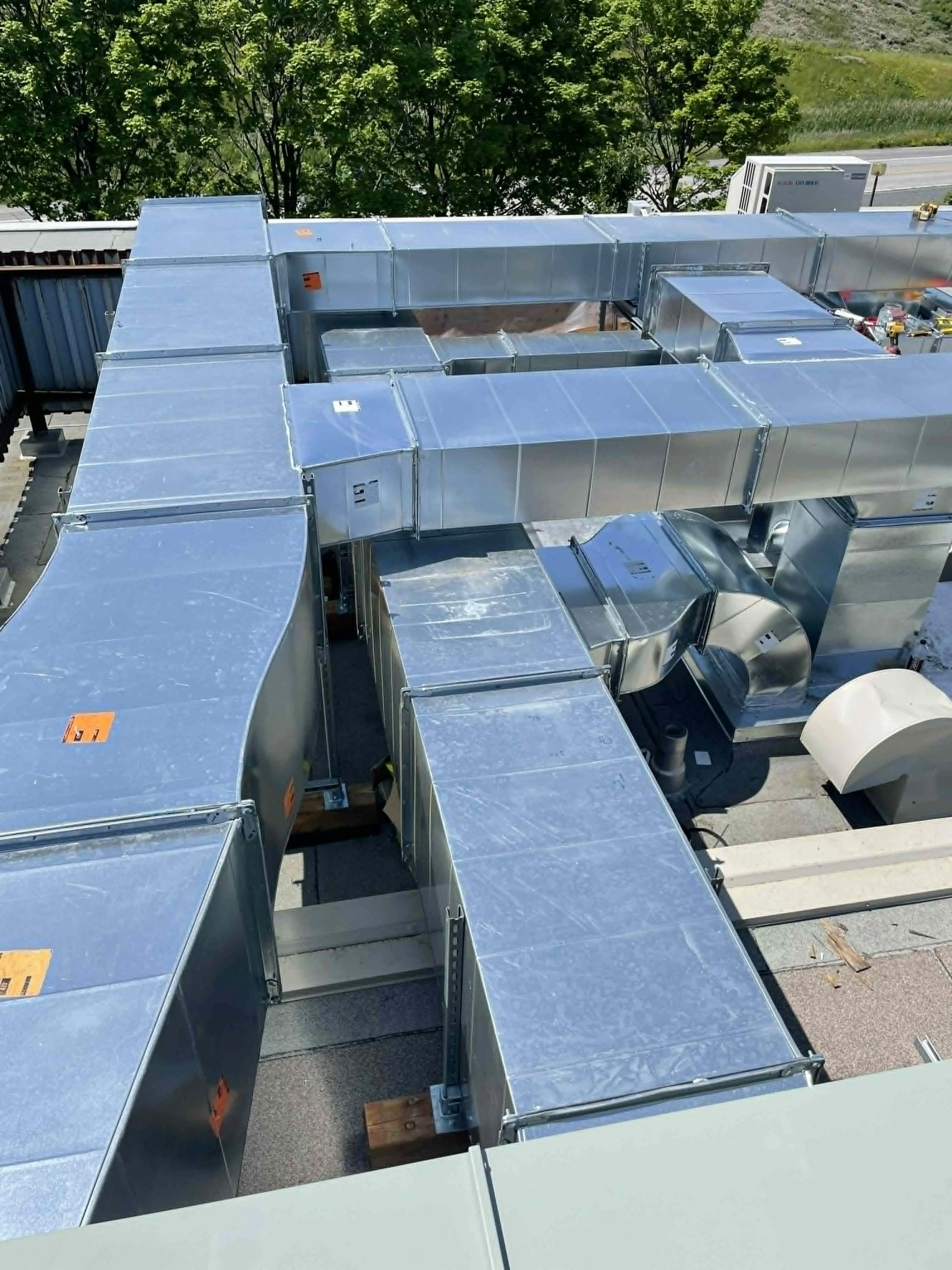 Vue aérienne d'un système de ventilation industriel en métal installé sur un toit, avec des arbres en arrière-plan.