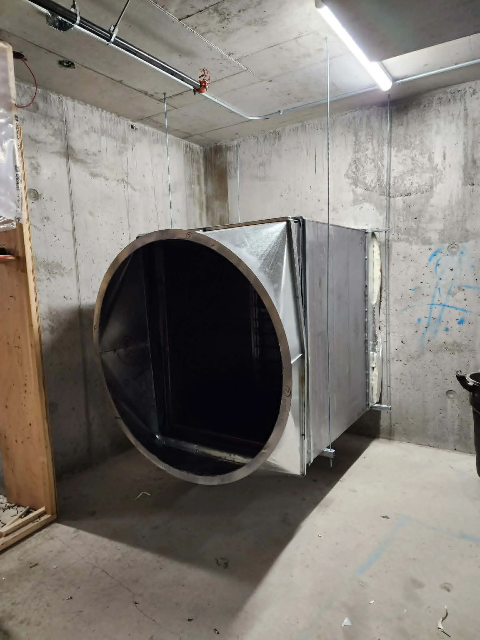Une machine industrielle en métal dans un espace en construction avec des murs en béton et un plafond en ciment. L'image est tournée de façon à ce que la machine apparaît de côté.