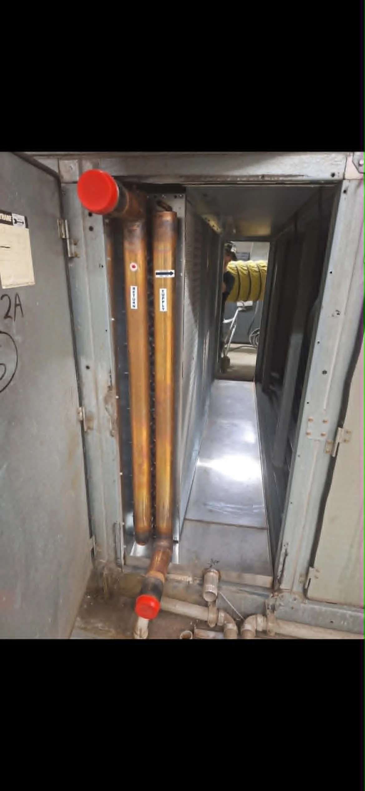 Vue d'une cloison technique avec des tuyaux en cuivre et des conduits en métal, dans une pièce technique ou une armoire électrique.