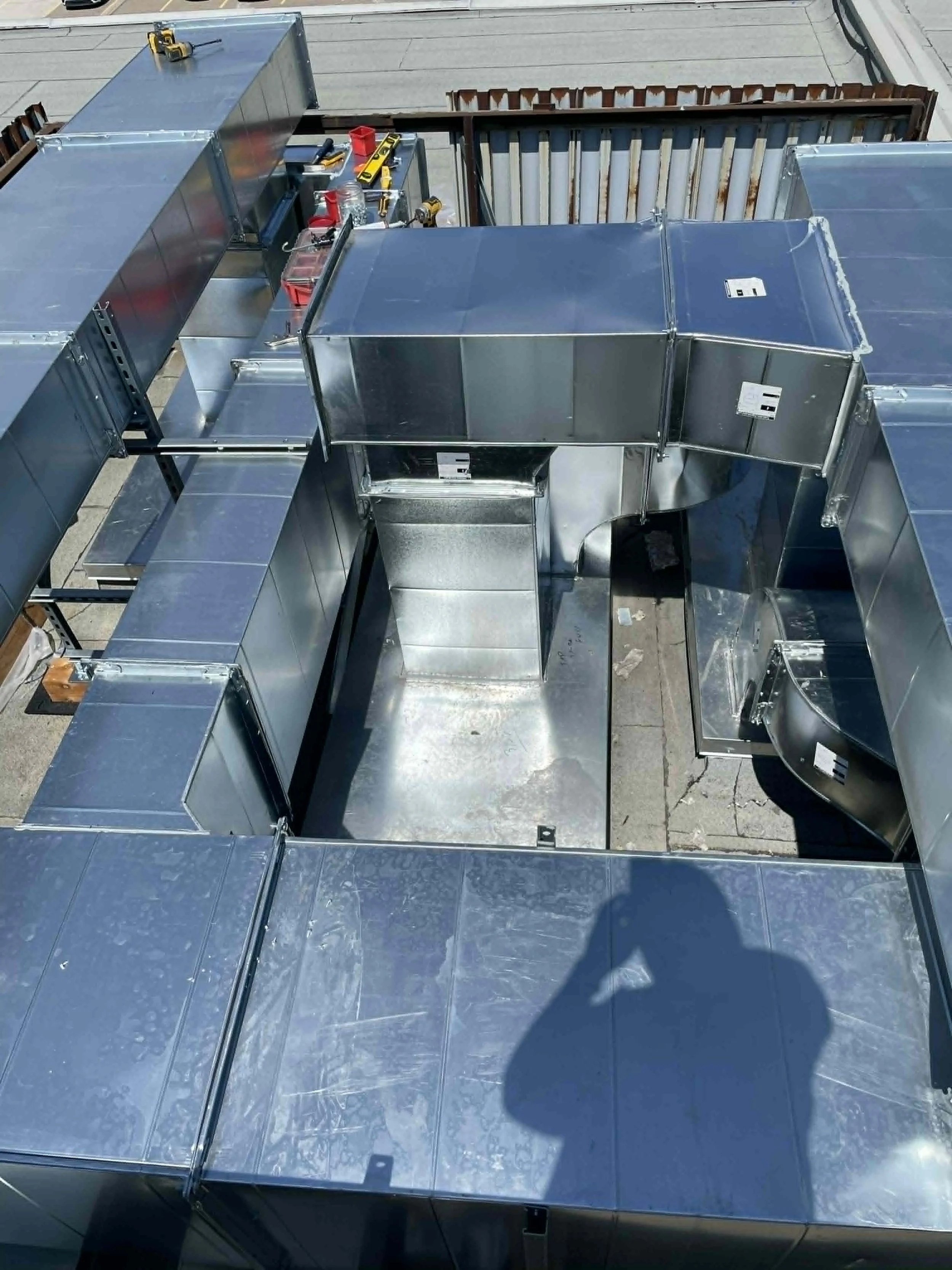Vue d'un ensemble de conduits en acier inoxydable posés sur un toit, avec des outils posés dessus, en cours d'installation.