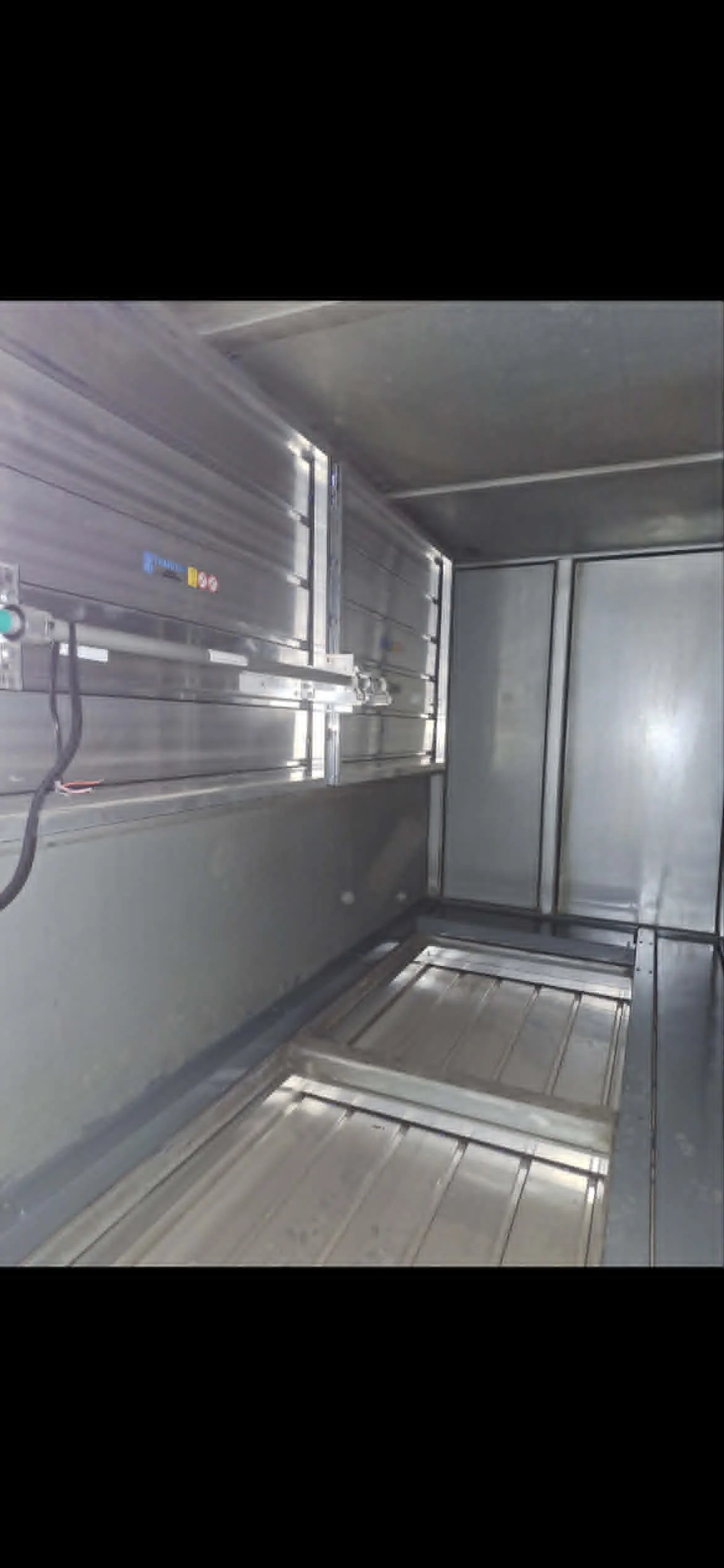Intérieur d'une cabine de camion en acier inoxydable, vide, avec des murs, un plafond, un plancher métallique et un mécanisme de verrouillage ou d'ouverture sur le mur.