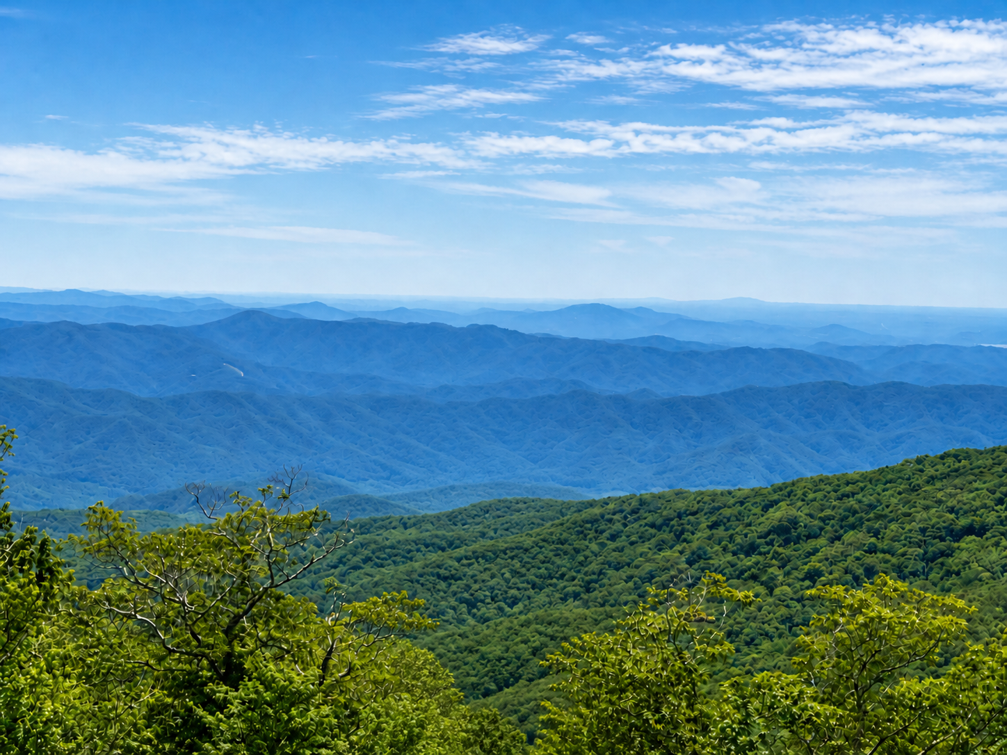 Scenic mountain view with forested hills and blue distant mountains beneath a partly cloudy sky.