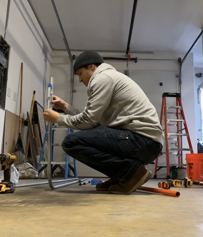 A person kneeling on the garage floor assembling furniture with tools around.