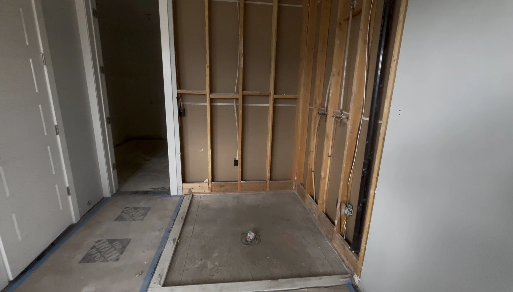 Interior of a room under construction with exposed wooden framing and electrical wiring, with a partially finished wall and doorway.