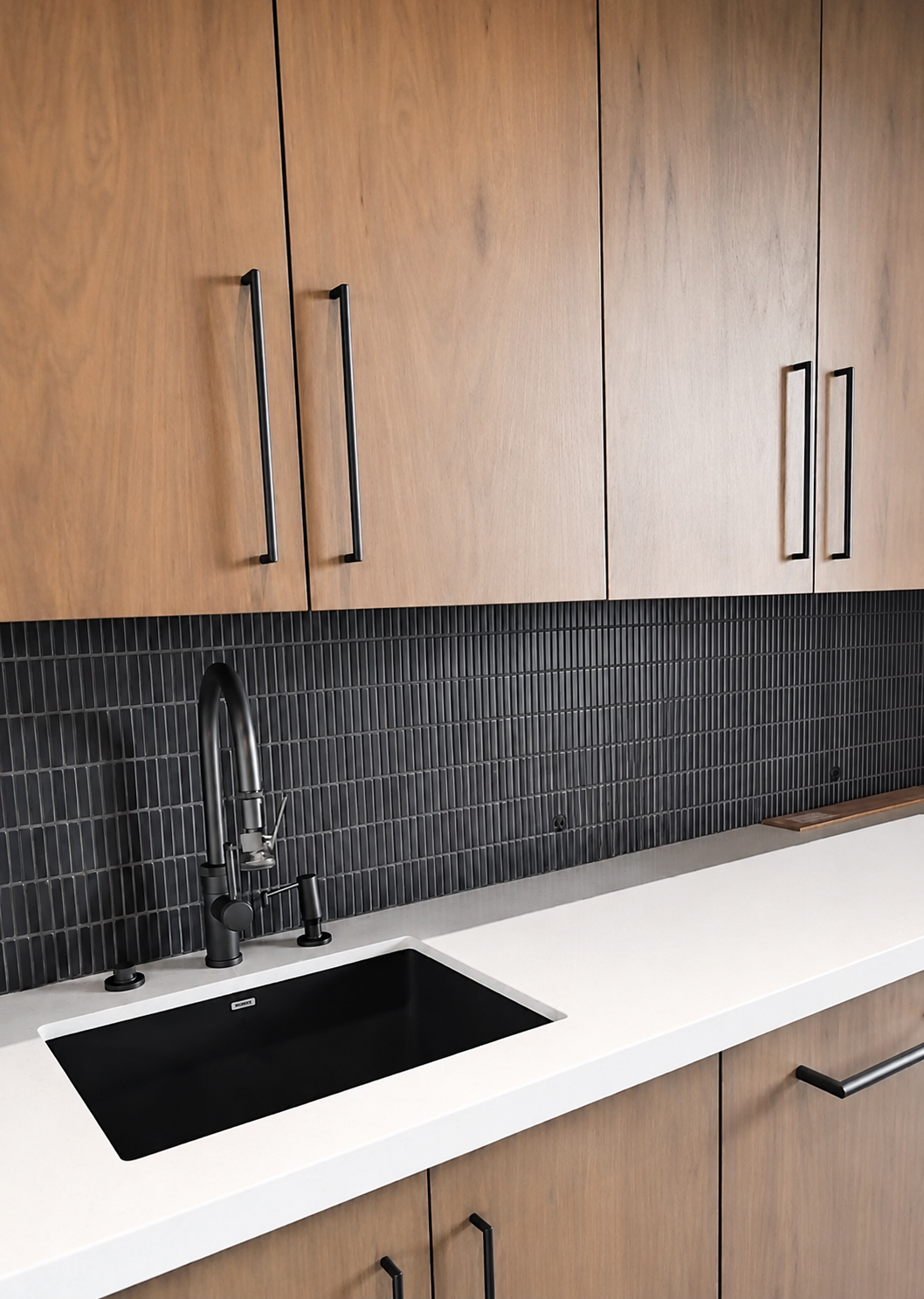 Kitchen with wooden cabinets, black tiled backsplash, black sink, and black faucet.