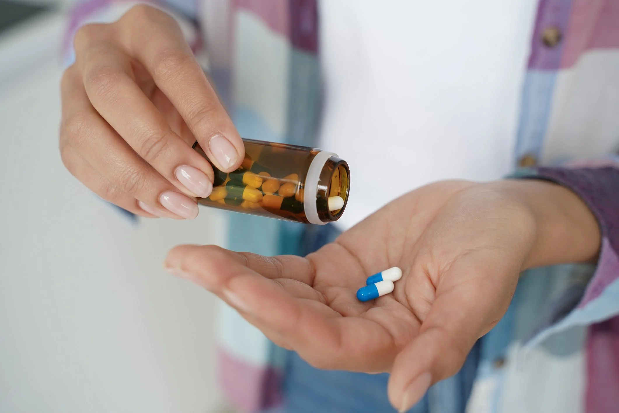 Person holding an orange pill bottle, pouring capsules into their hand.