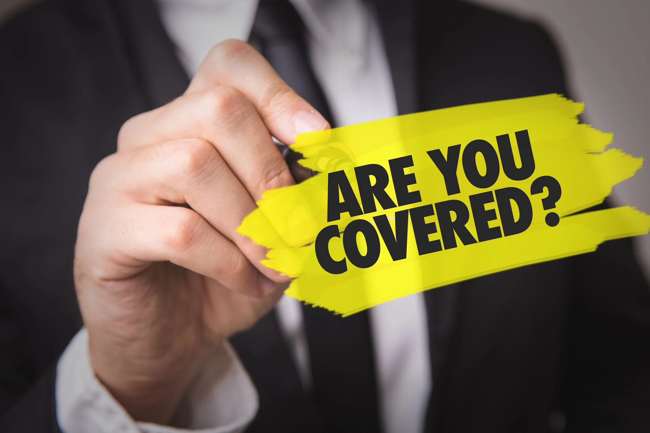 A person in a suit holding a torn yellow paper with the words "Are you covered?" printed on it.