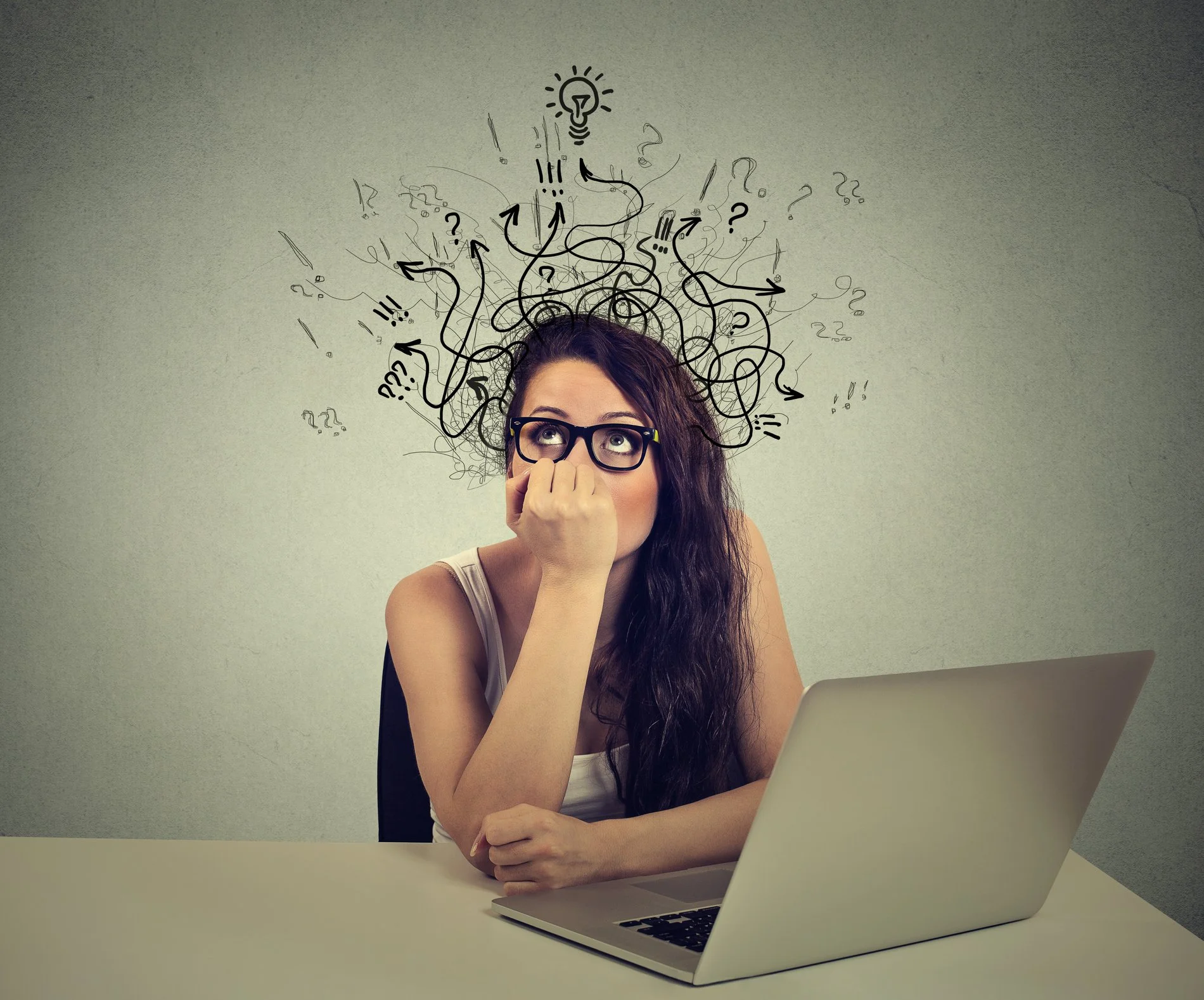 A woman with long dark hair, wearing glasses, sits at a desk with a laptop in front of her. She has her hand on her face, looking up thoughtfully. Above her head are doodles of question marks, arrows, and a lightbulb symbol, indicating she is thinking or brainstorming.
