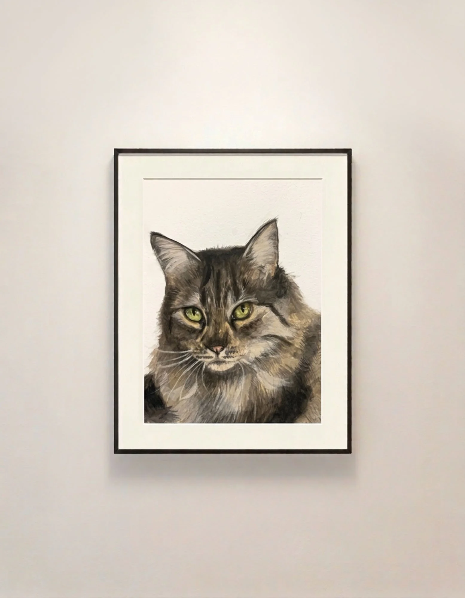 Framed watercolor and gouache realistic painting of a long-haired brown and black cat with green eyes on a white gallery wall.