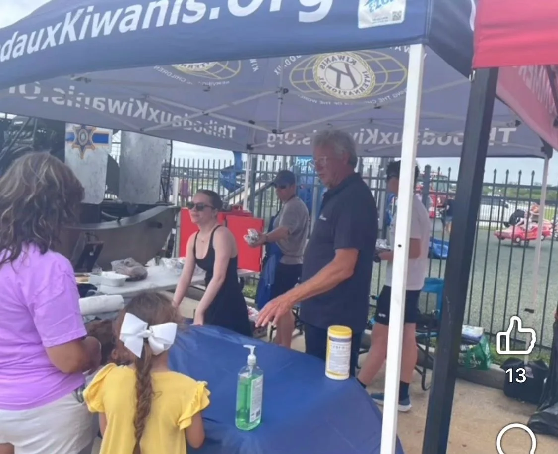 People at a booth or food stand outdoors with Robert Theriot serving the public.