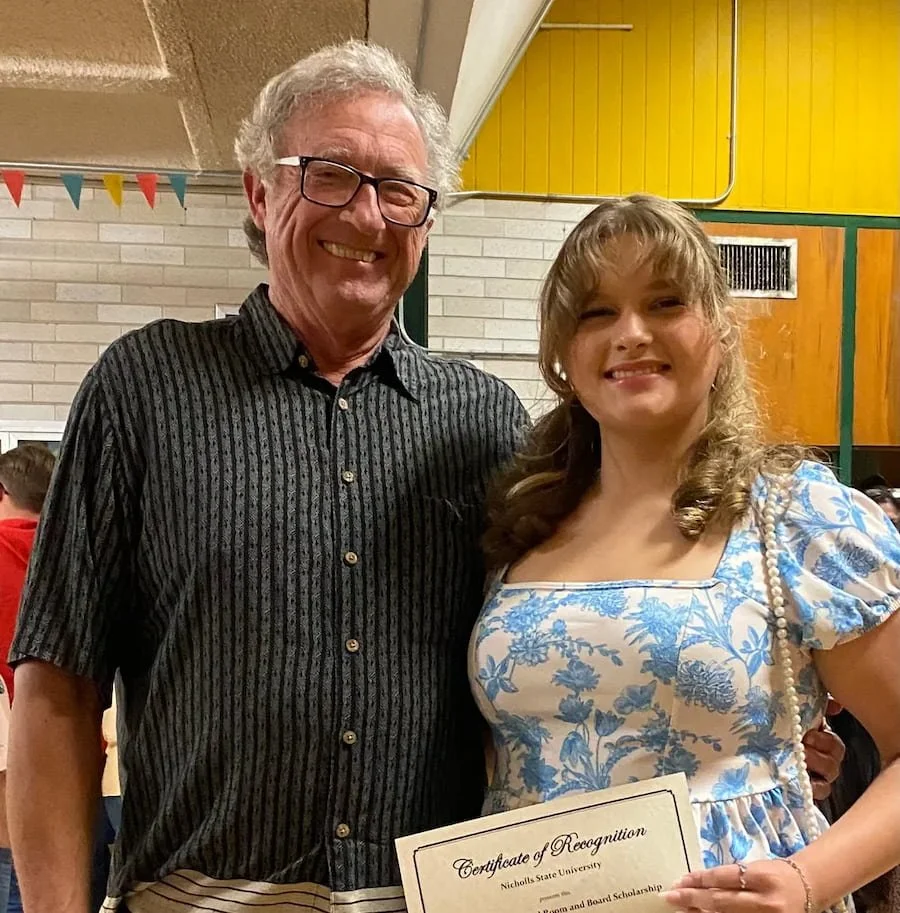 Robert Theriot and his granddaughter holding a certificate at an indoor event.