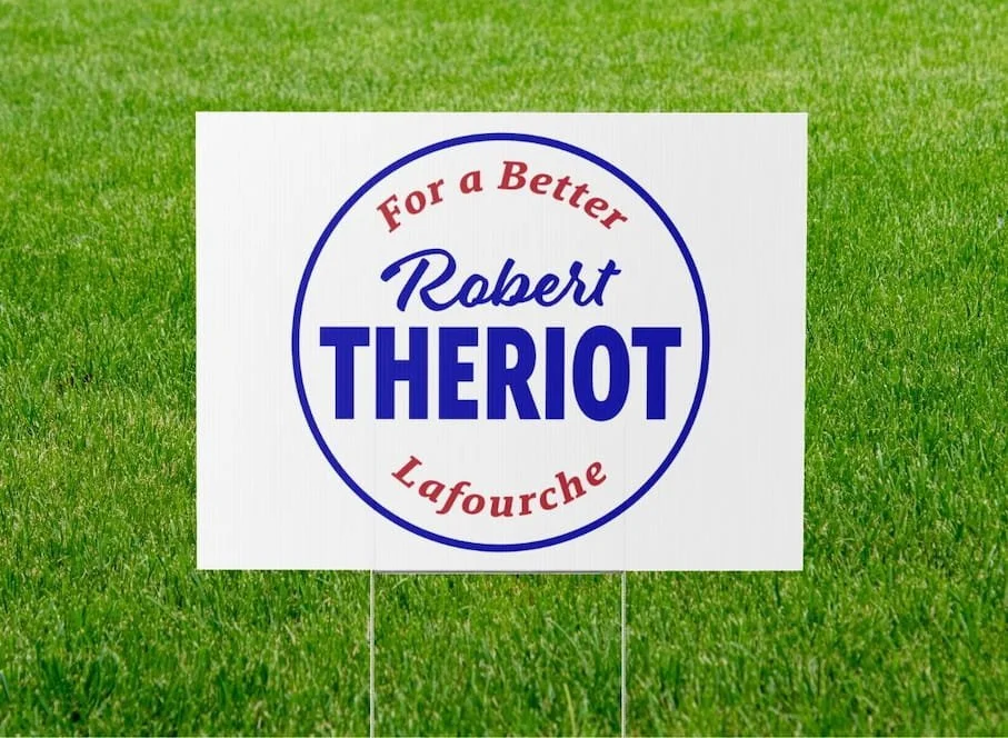 Political campaign sign supporting Robert Theriot for Lafourche with a white background and red and blue text, placed on green grass.