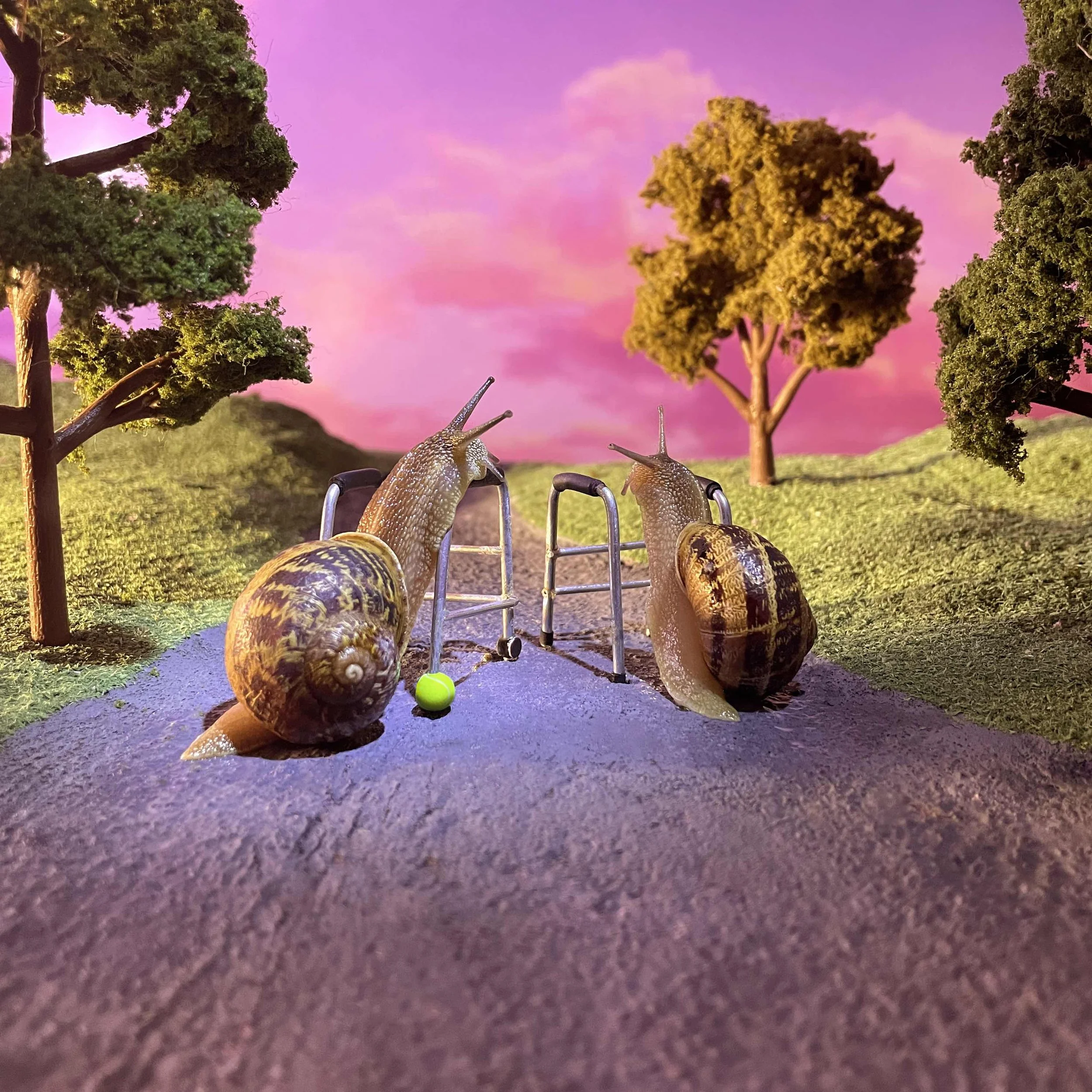 Close-up of a miniature outdoor scene with trees, a purple sky, and small snail figurines on a textured surface.