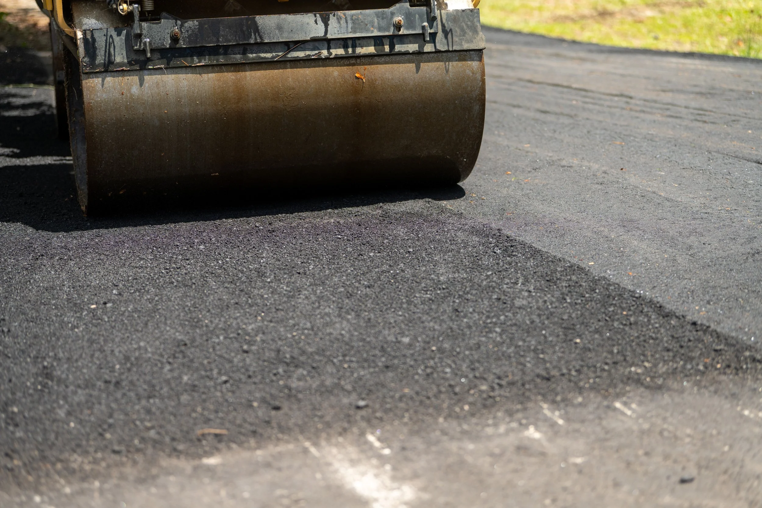 A close-up of a road roller compacting asphalt on a newly paved road during daytime.