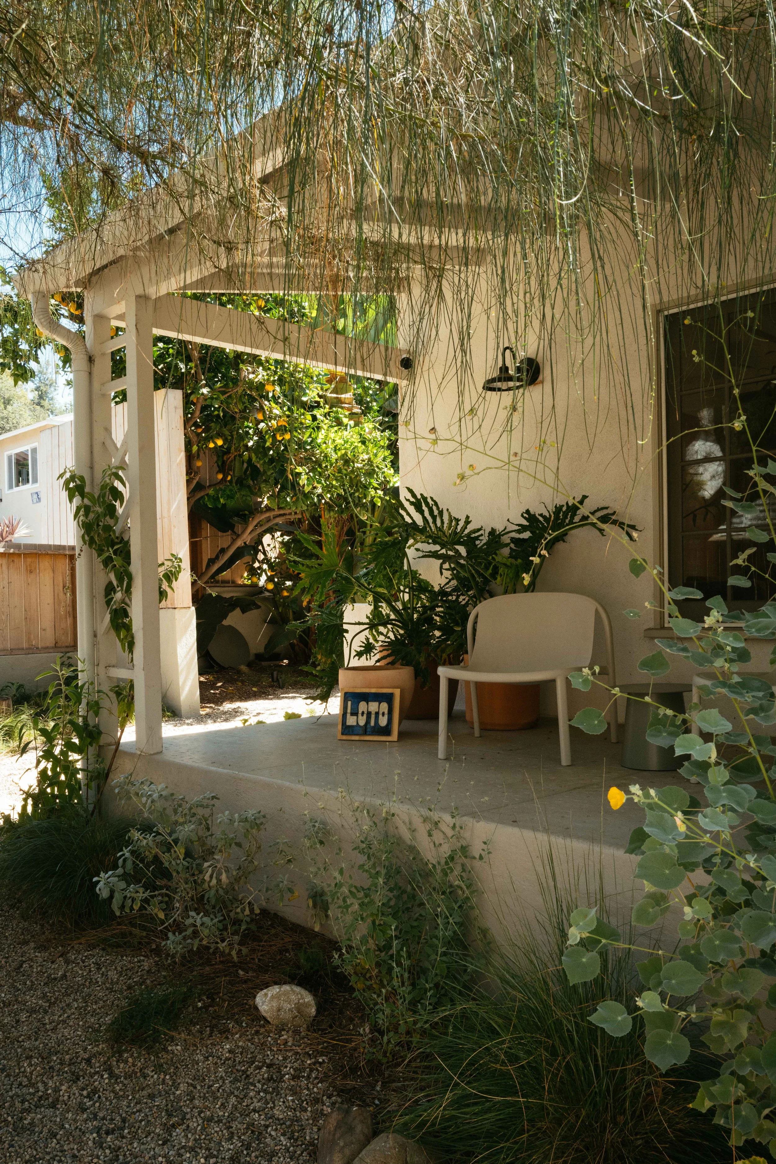 Backyard patio with hanging plants, greenery, a wooden fence, a chair, and a small 'Loto' sign.