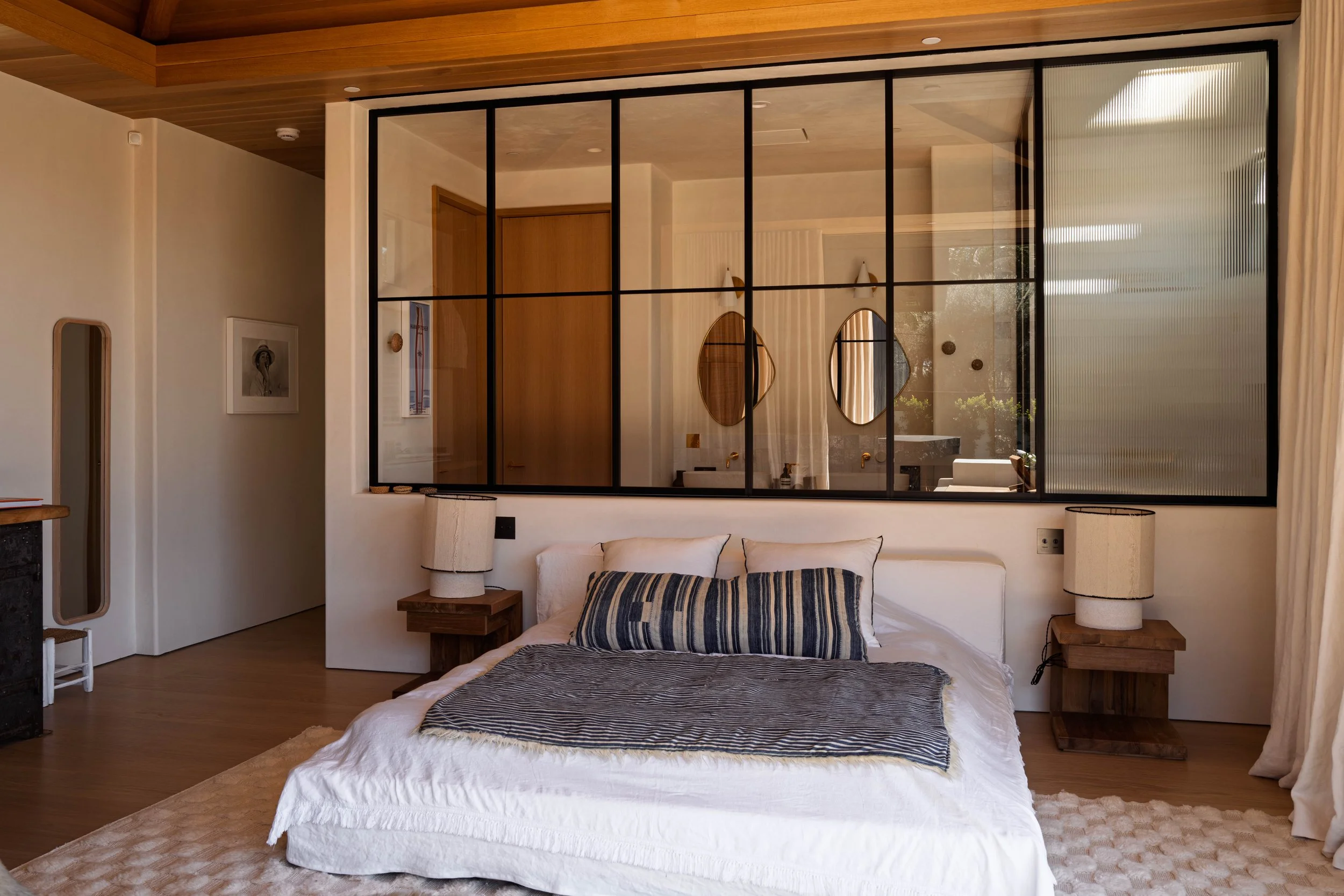 Bedroom with steel-framed glass partition and striped pillows, Point Dume home by Peggy North
