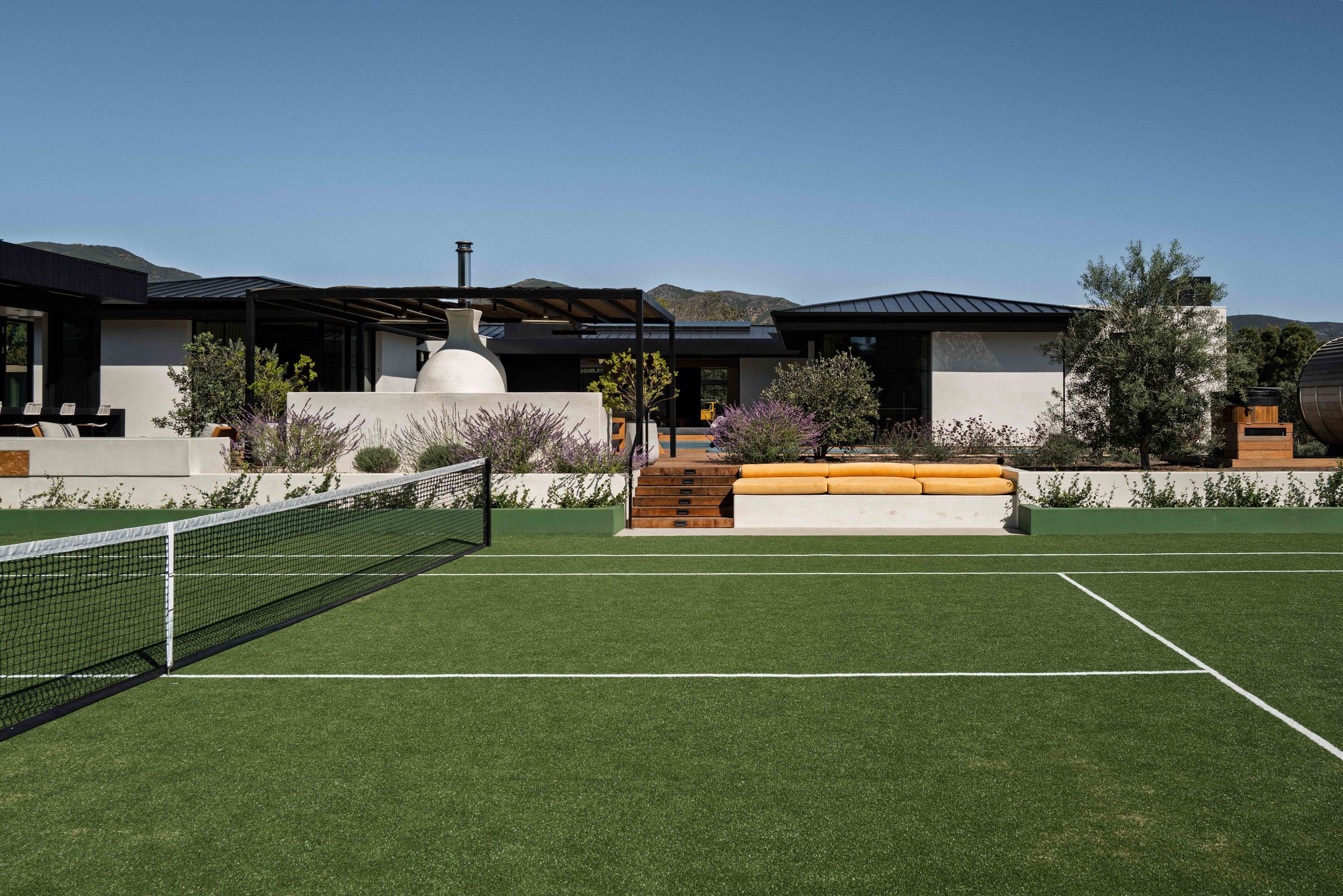Grass tennis court in front of the house with yellow lounge cushions, Point Dume Malibu