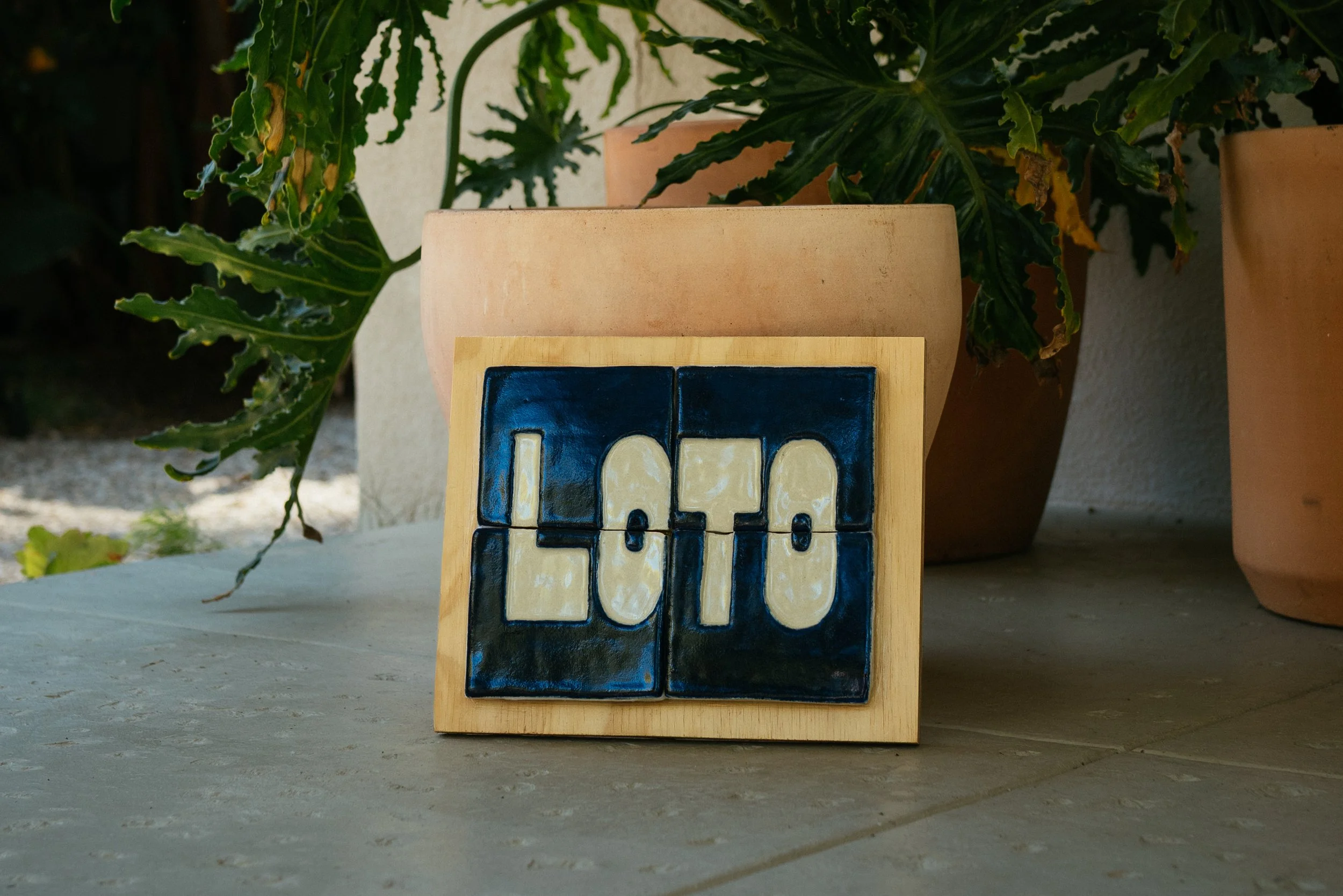 A wooden block with a blue and yellow train design next to large potted plants with green leaves.