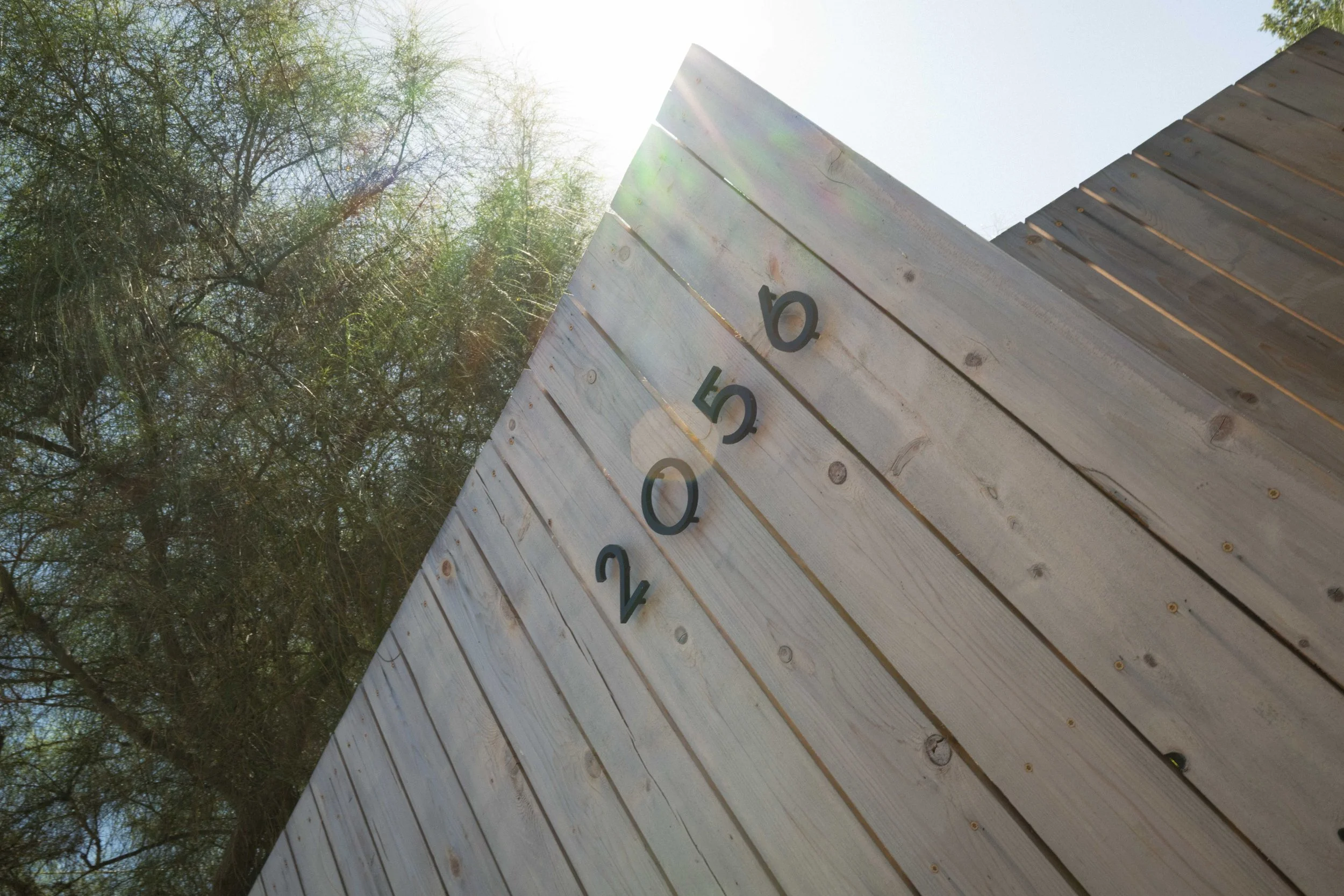 Close-up of a wooden fence with numbers on it, outdoors on a sunny day with trees in the background.