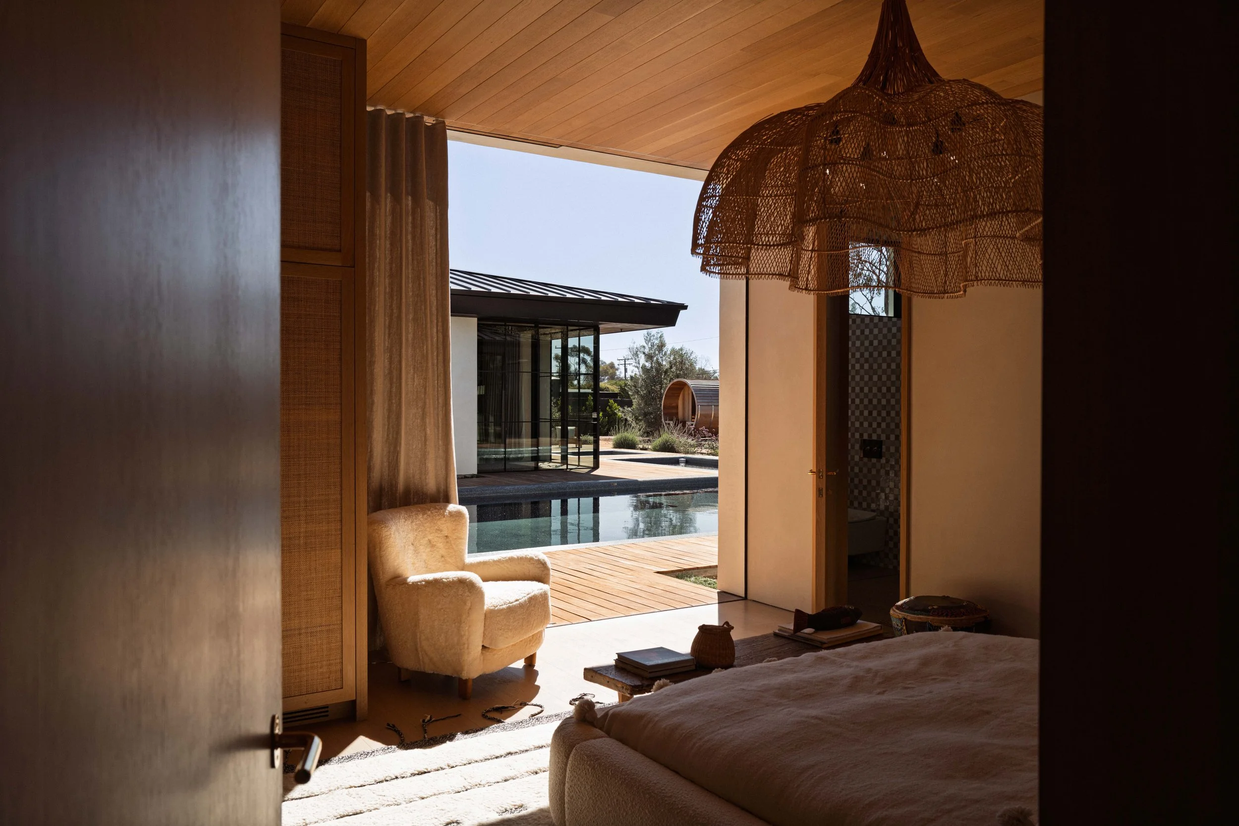Bedroom corner with armchair and woven pendant opening onto the pool, Malibu home