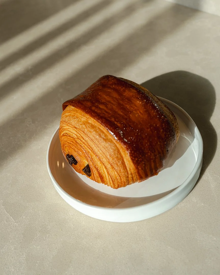Pain au chocolat on a white plate in afternoon sun, Louma Bakery