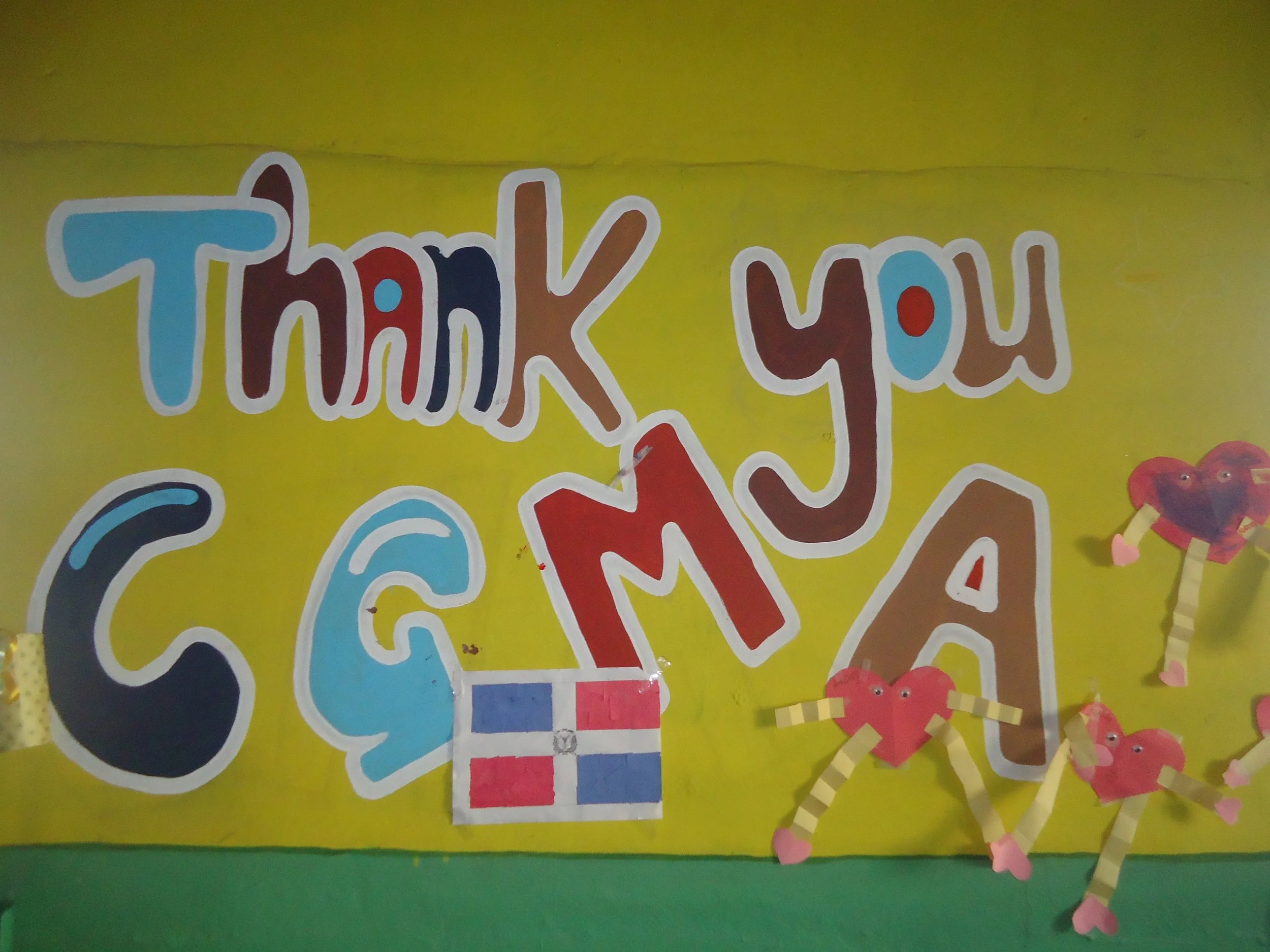Decorative display with colorful cutouts and handwritten messages on a bright green background, featuring the partially visible phrase 'Thank You'.